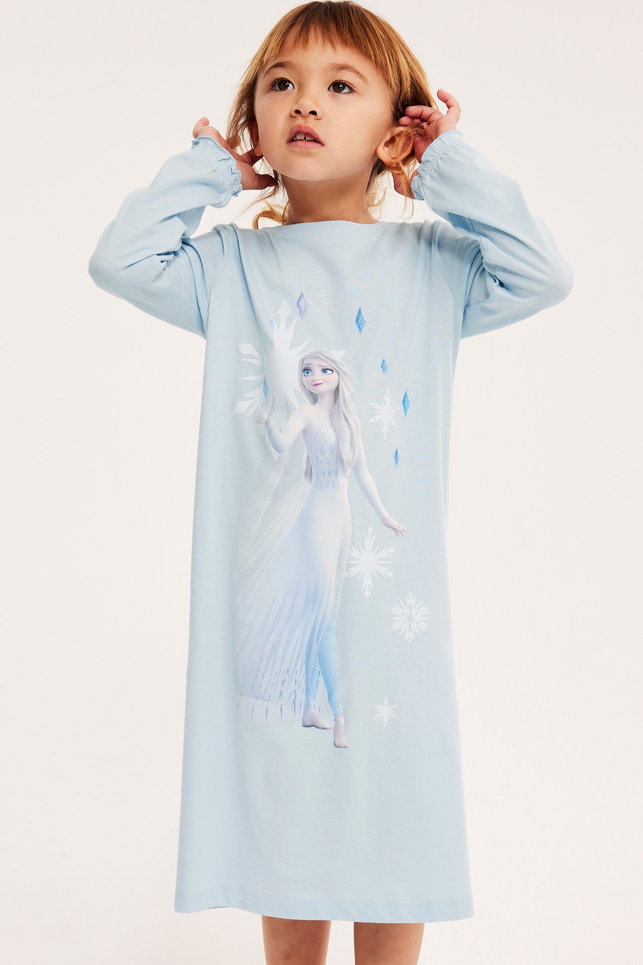 Forfra, et barn i lyseblå langermet nattkjole med Elsa-trykk.