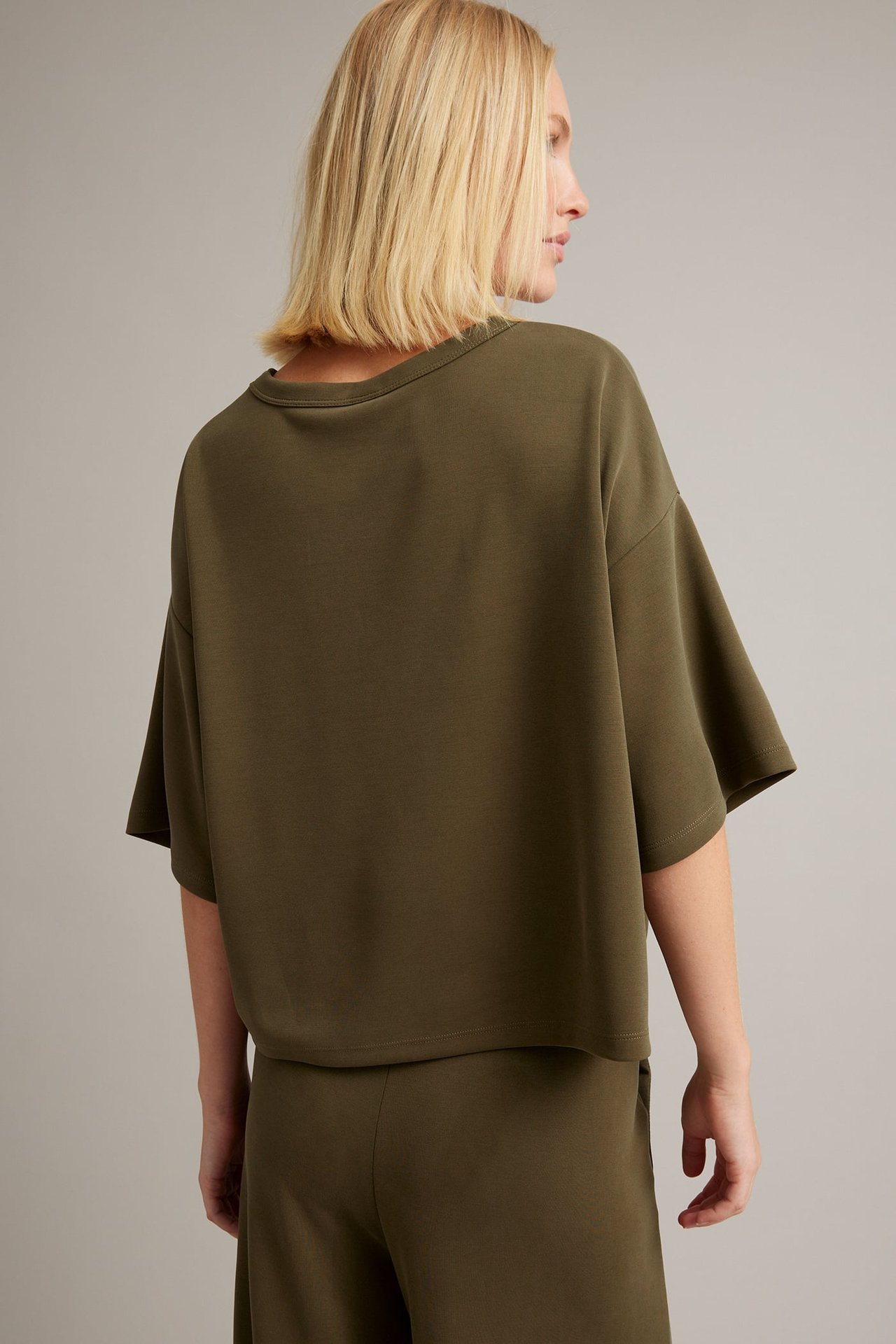 Kvinnlig modell, bakifrån, bär mörk olivgrön oversized kortärmad croppad topp och matchande byxor.