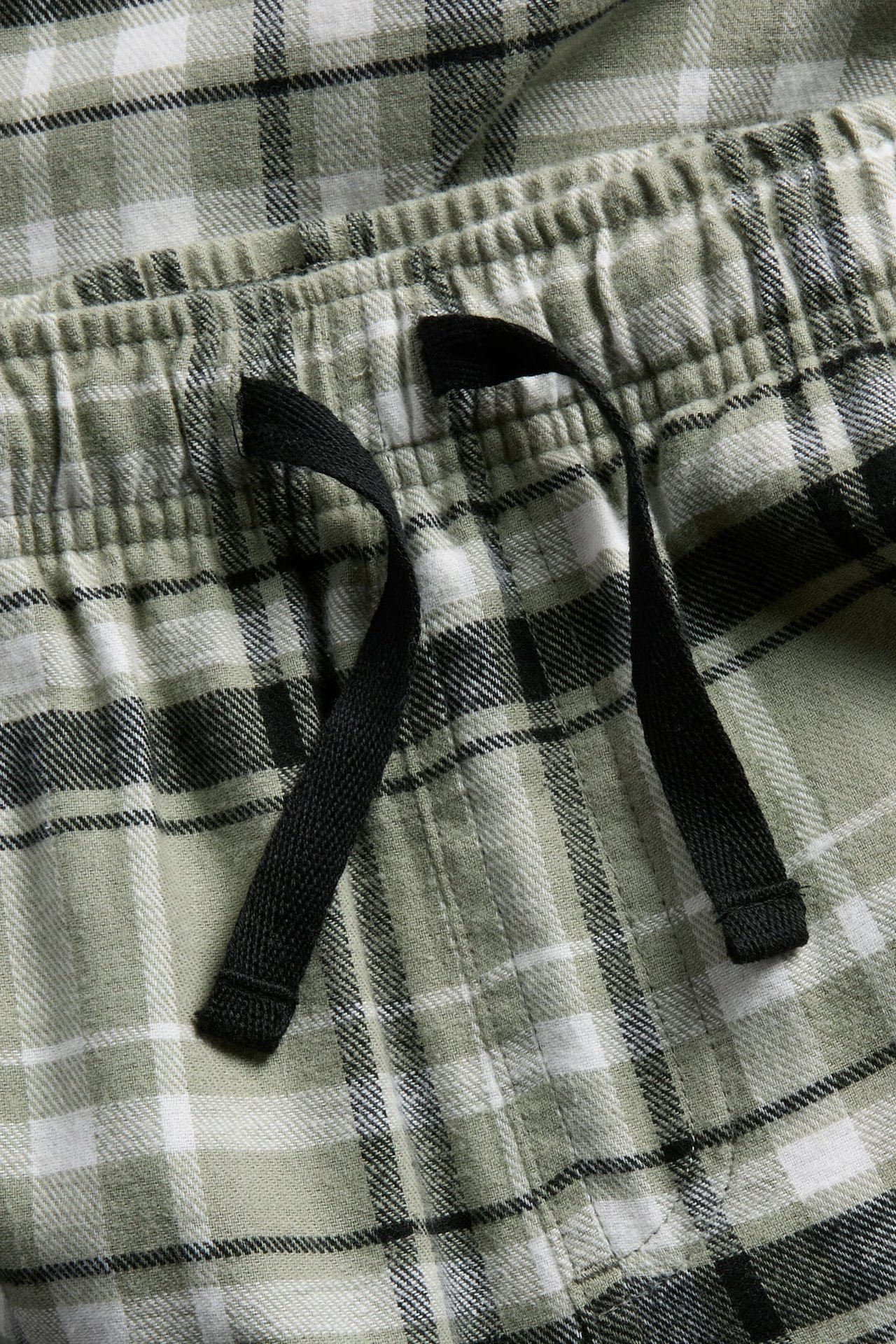 Lähikuva vihreä-, valko- ja mustaruudullisista pyjamahousuista, joissa musta kiristysnyöri.