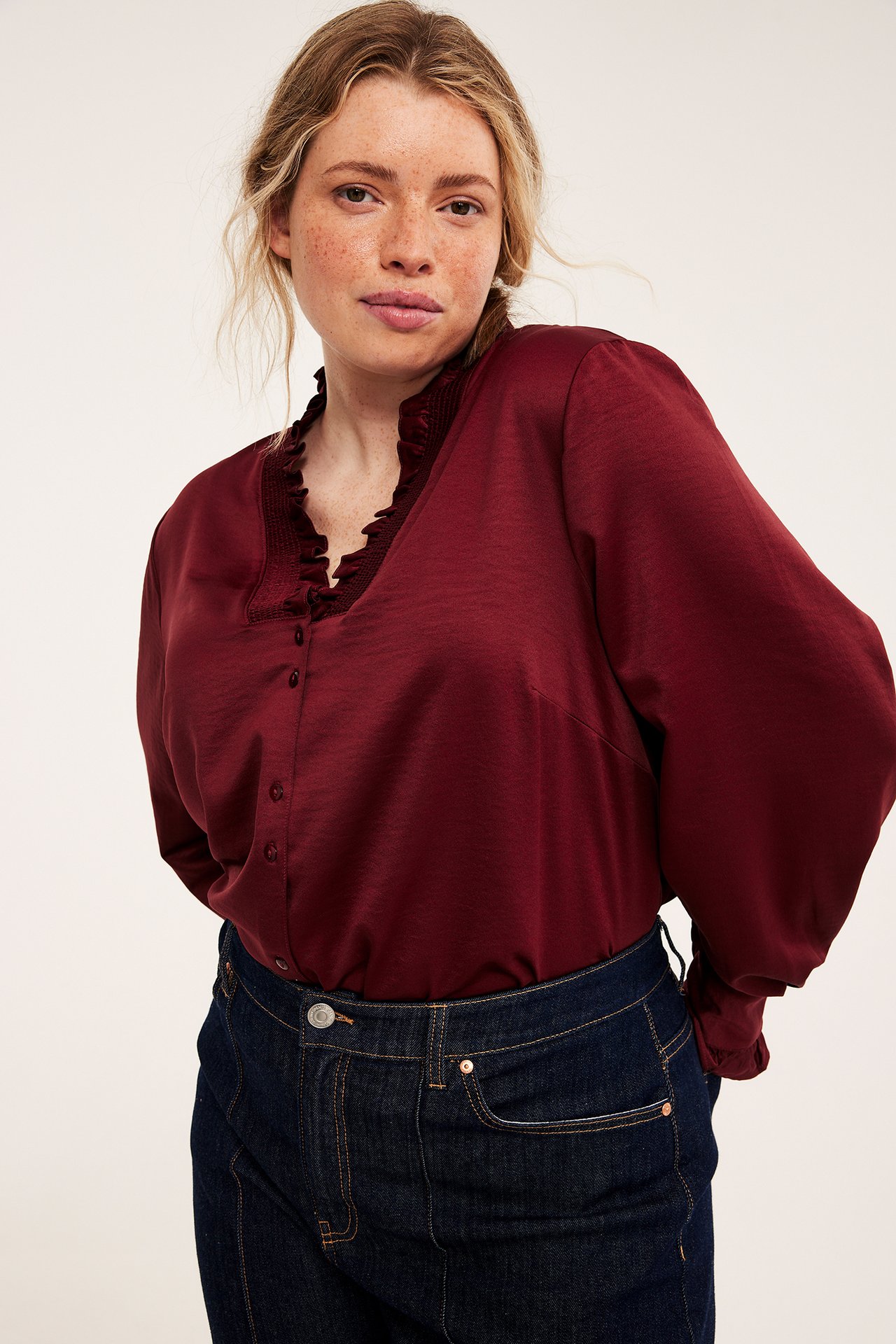 Framifrån, mörkröd volangblus med långa ärmar och mörkblå jeans.