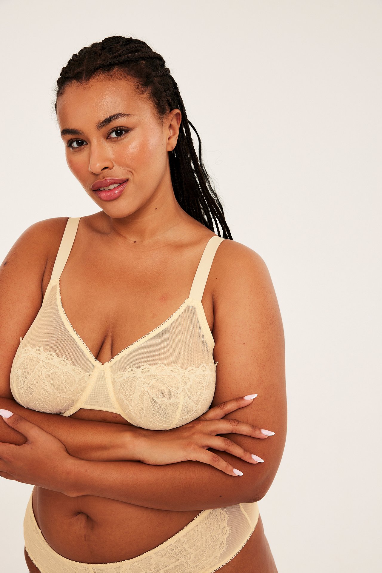 Framifrån på en kvinnlig modell i en ljus beige spets-bh och matchande trosor.