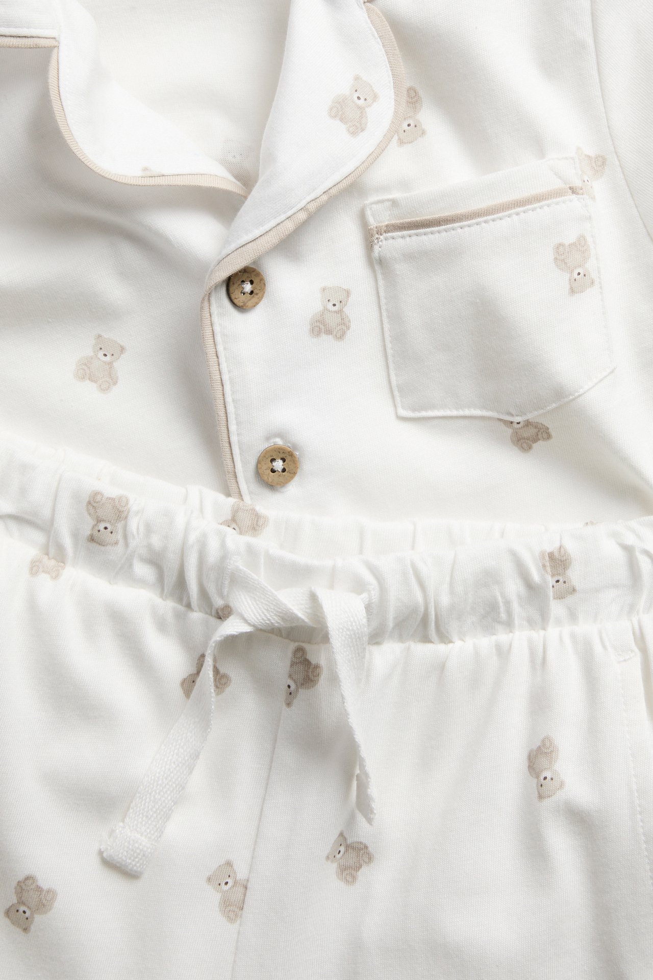 Lähikuva valkoisesta vauvan pyjamasetistä, jossa on beige nallekuvio ja napit.