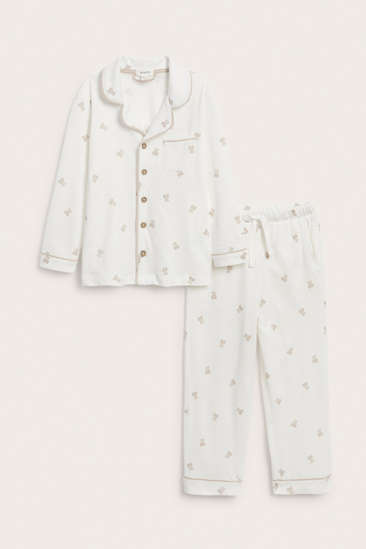 Valkoiset vauvan pyjamat ruskealla nallekuviolla ja koristesaumoilla, edestäpäin.