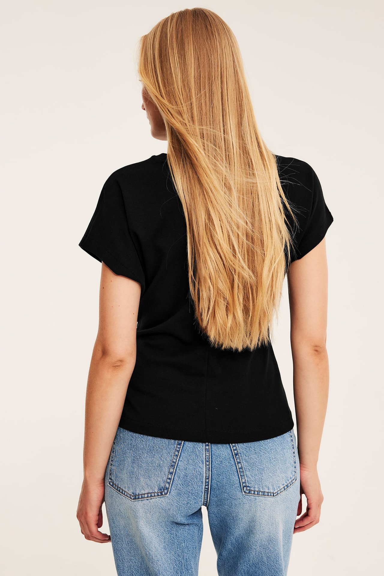 Bakfra av kvinne i svart kortermet t-skjorte og lyseblå jeans.