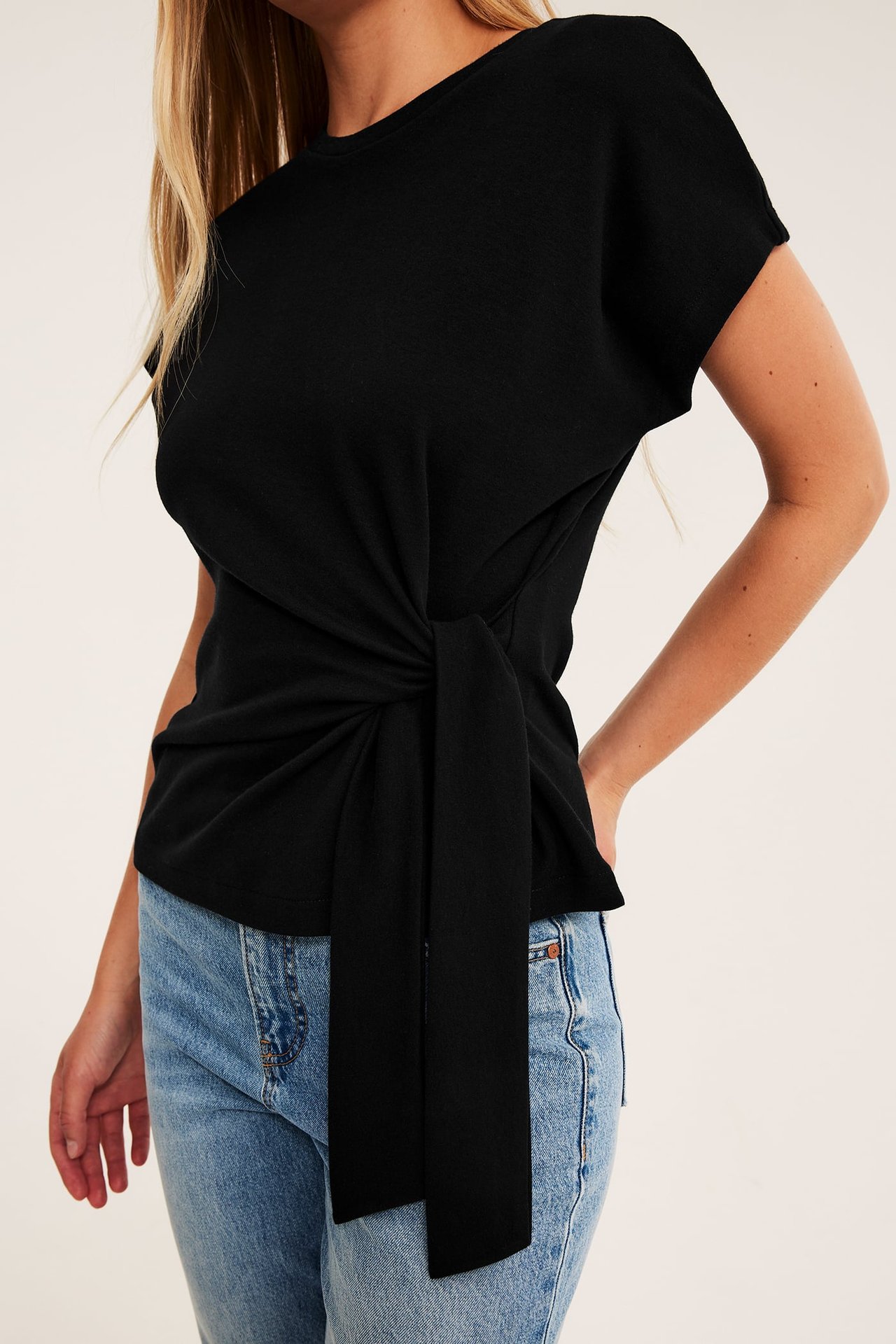 Forfra: Kvinne med svart kortermet topp med knyting foran og blå jeans.