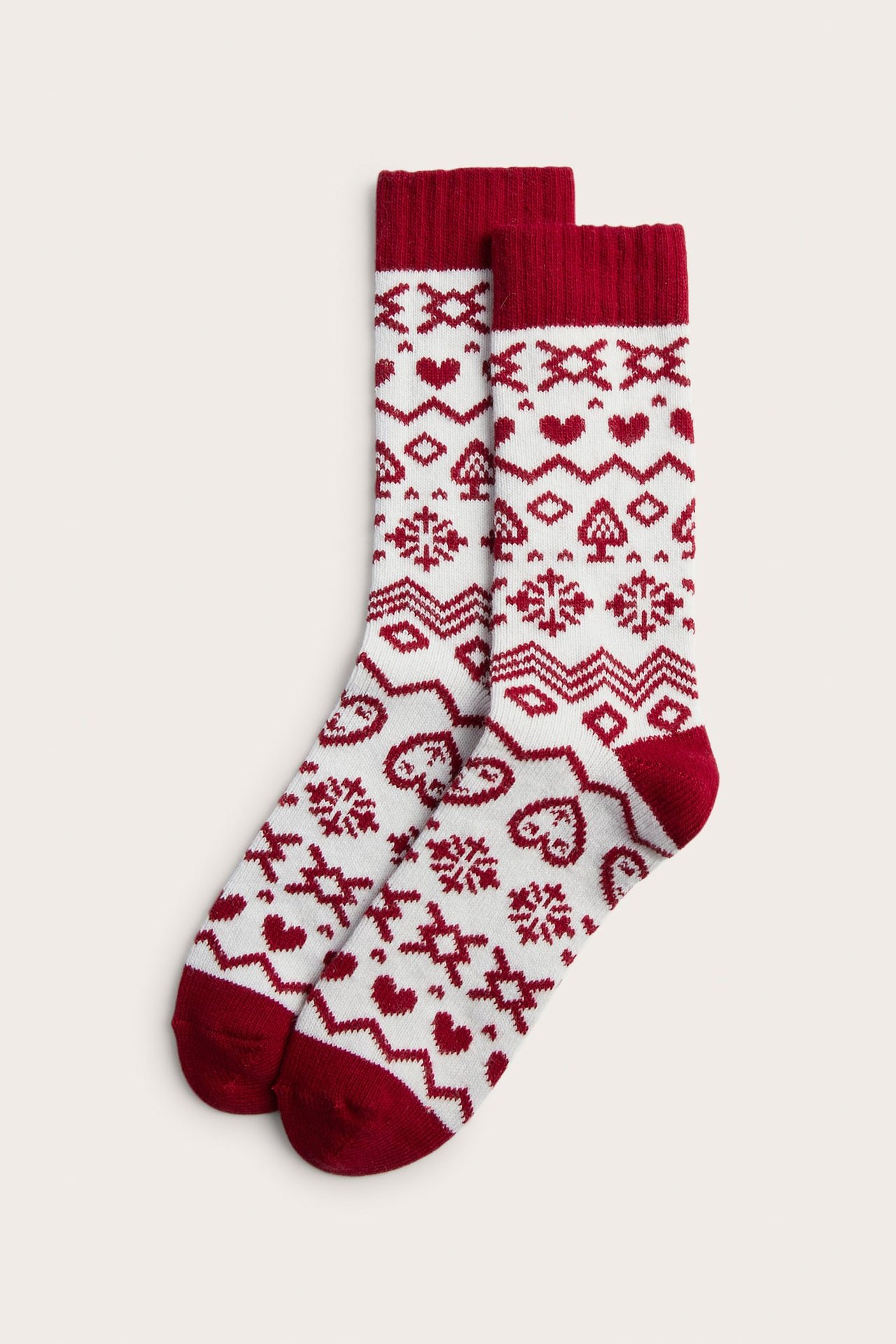 Uppifrån sett par vita och röda Fair Isle-sockor med hjärtan, spader och snöflingsmönster.
