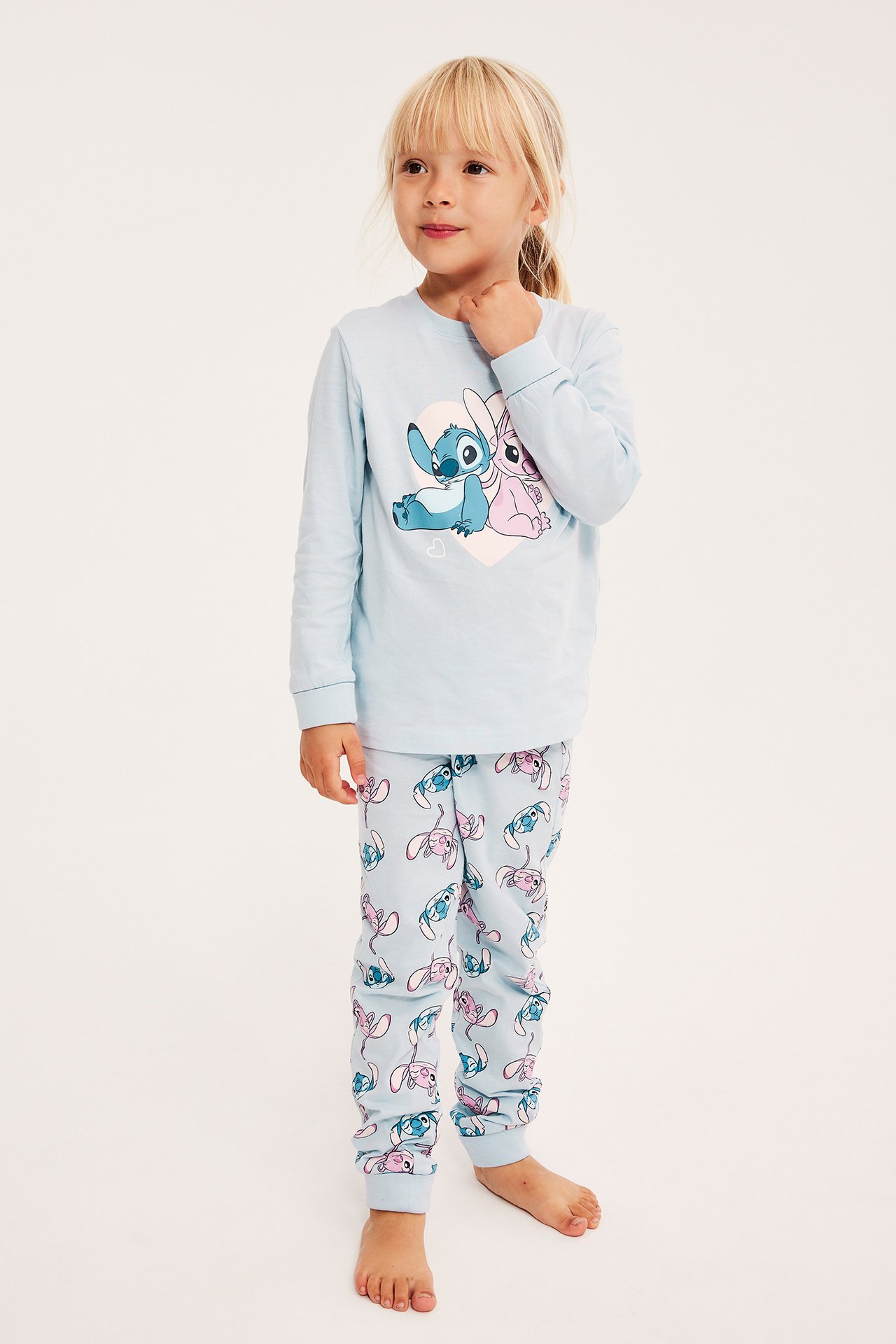Forfra av et barn i lyseblå langermet pyjamas med Stitch og Angel karaktertrykk.
