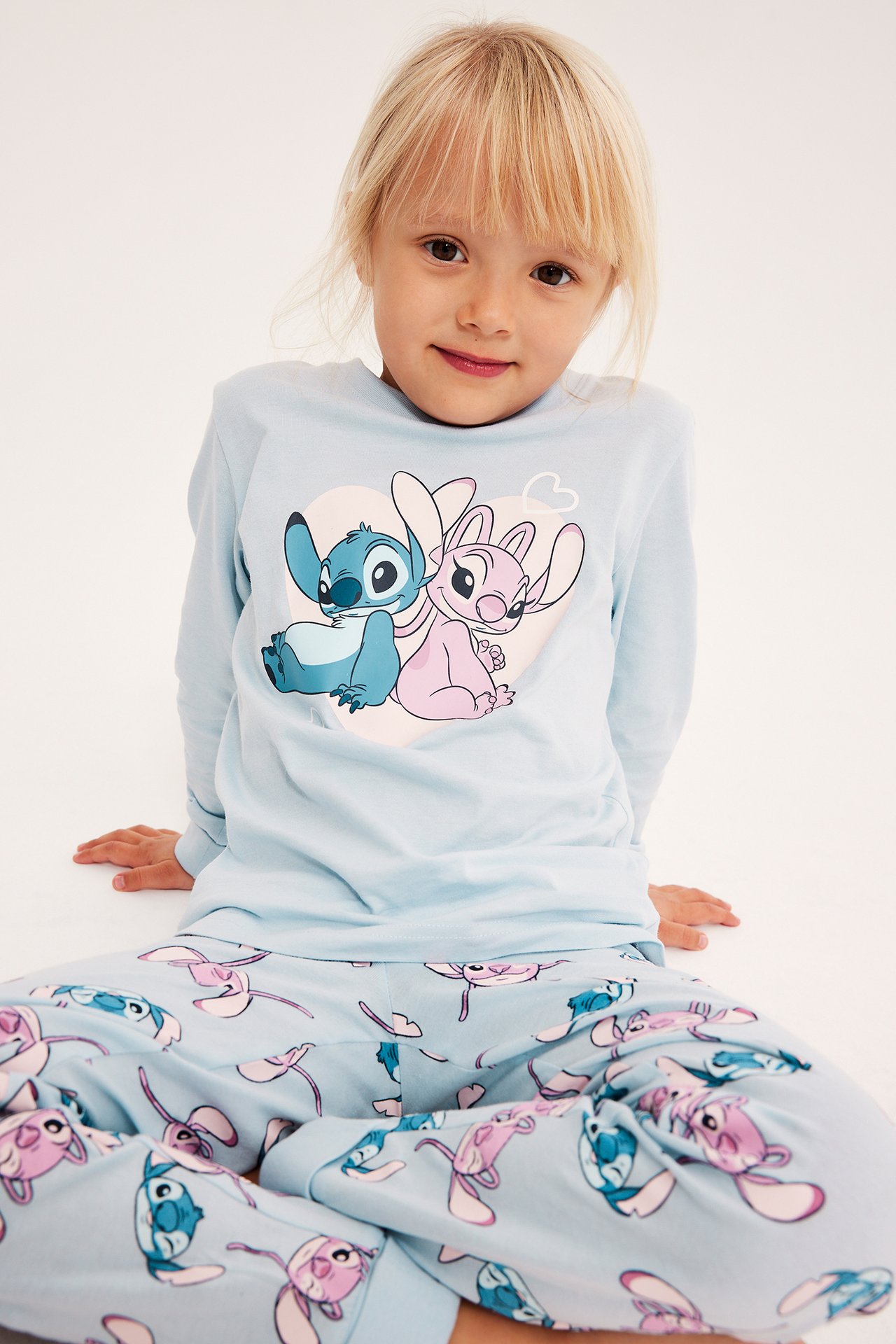 Front av et barn som har på seg et lyseblått Stitch og Angel-mønstret pyjamas sett.