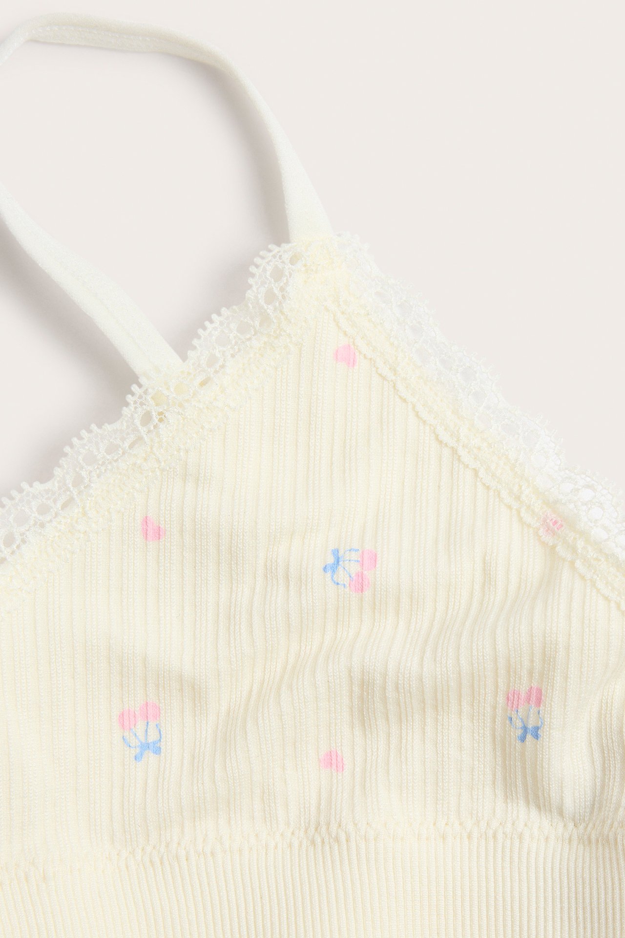 Närbild på en ljusgul ribbad bralette med spetskant, rosa hjärtan och blå rosetter.