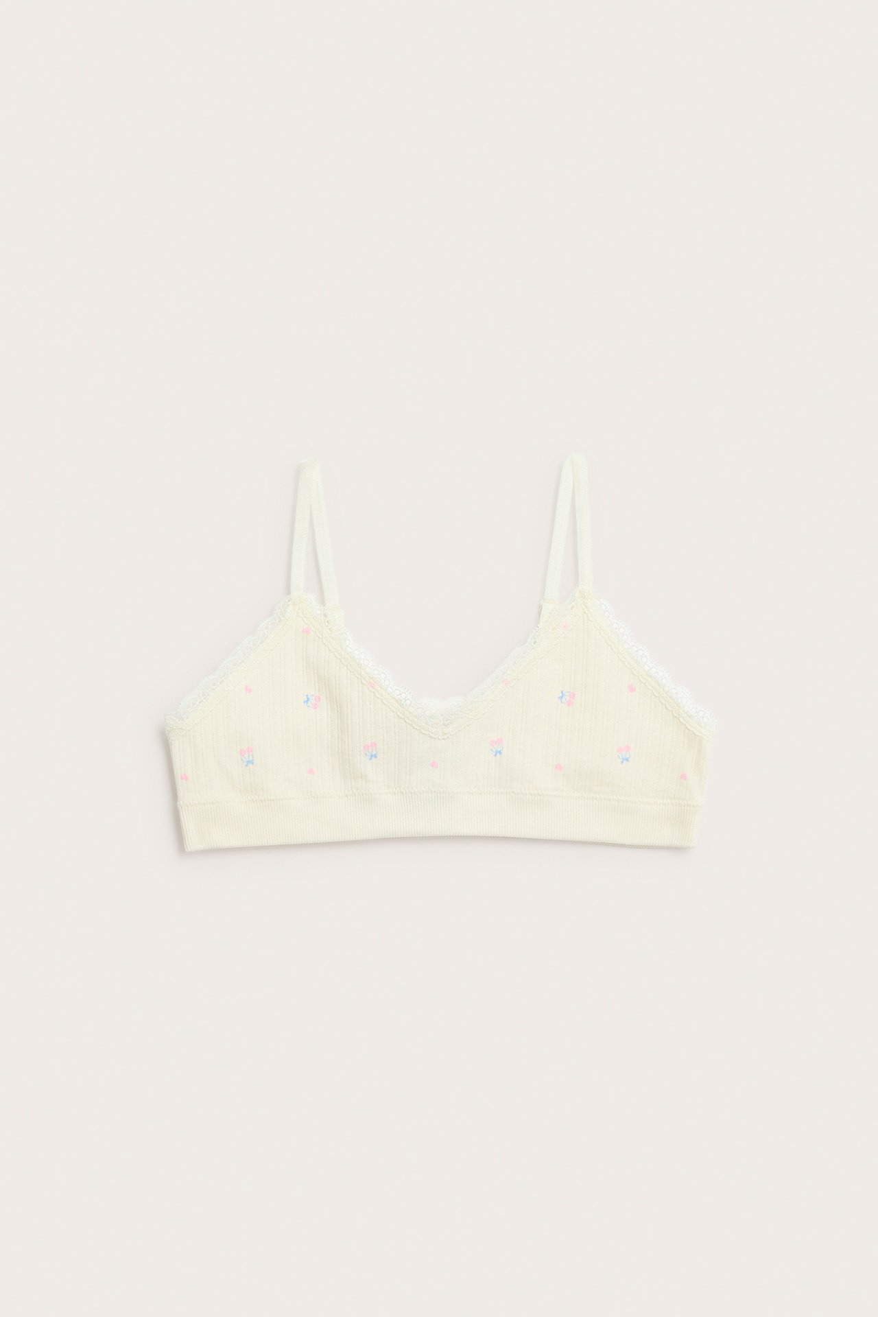Vaaleankeltainen ribattu bralette, jossa vaaleanpunaisia/sinisiä rusetteja ja pitsireuna, edestä.