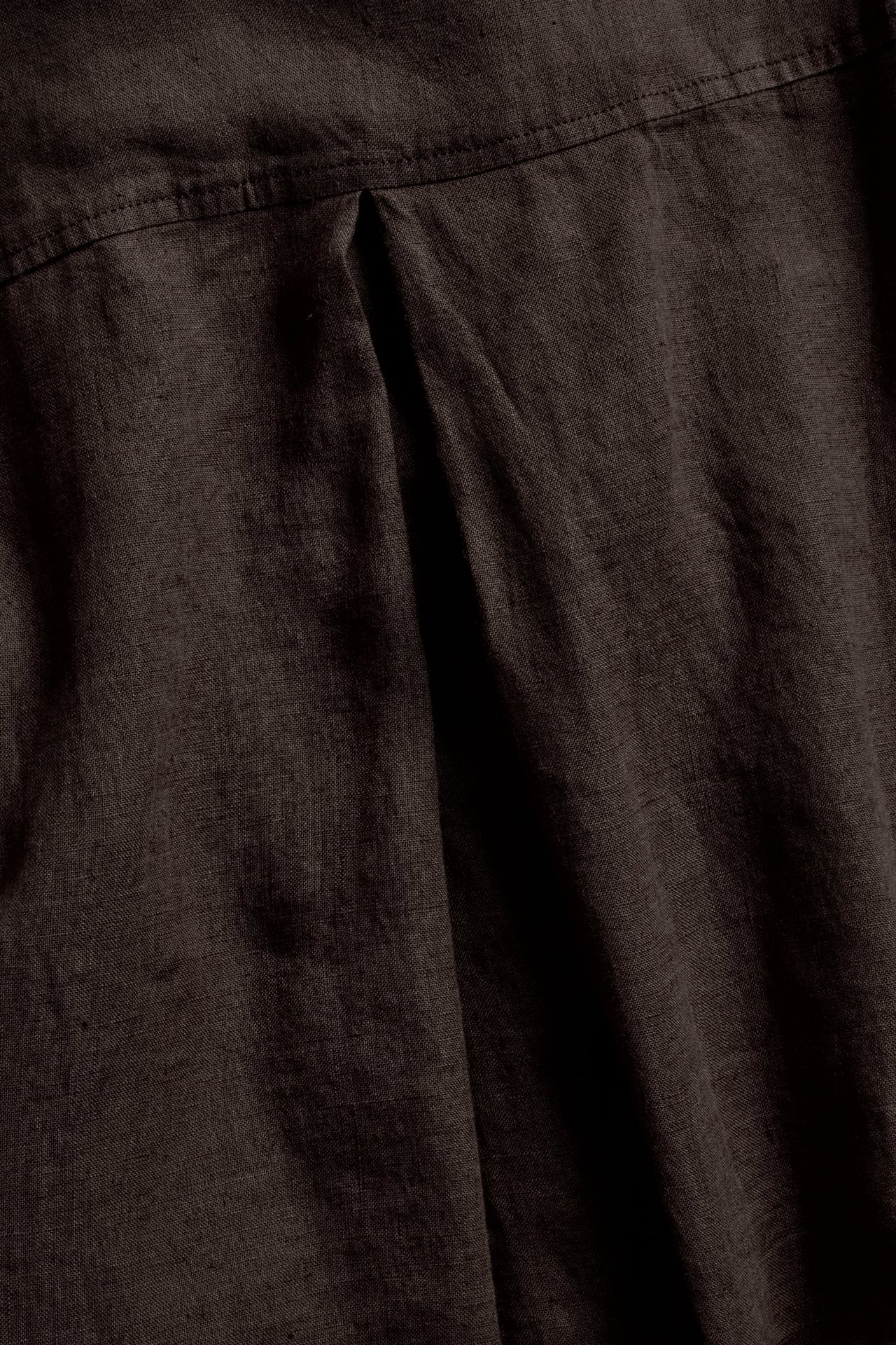 Nærbilde av en mørkebrun oversized linskjorte, som viser et tydelig plissé i stoffet.