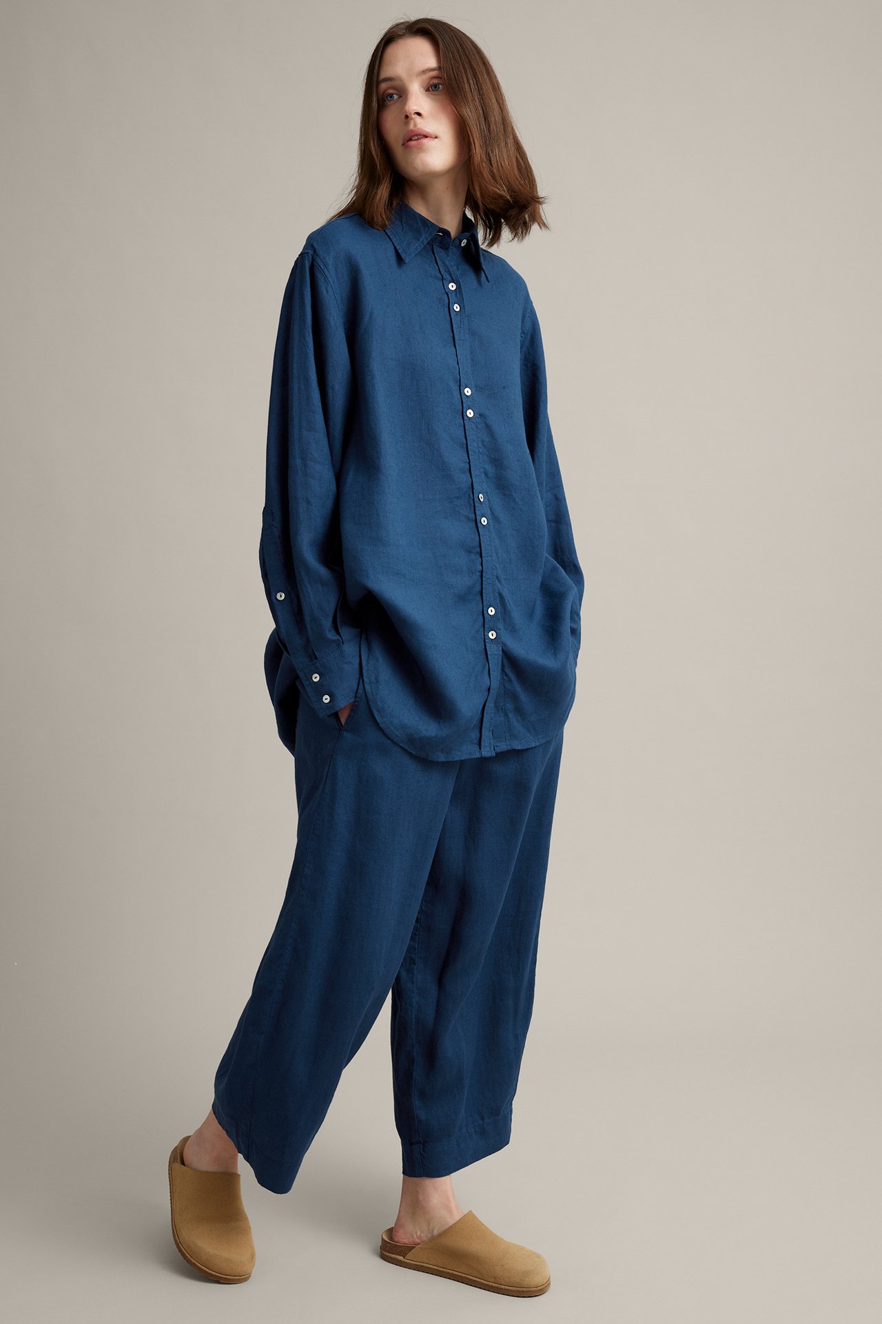 Framifrån: Kvinna i oversized blå linneskjorta, matchande vida byxor och ljusbruna mules.