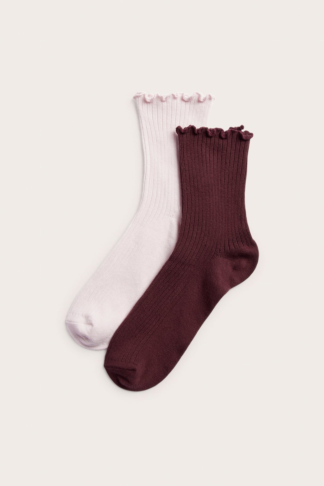 Ylhäältä näkymä ribbineulotuista sukista, joissa röyhelöreunat, yksi vaaleanpunainen, yksi burgundinpunainen.