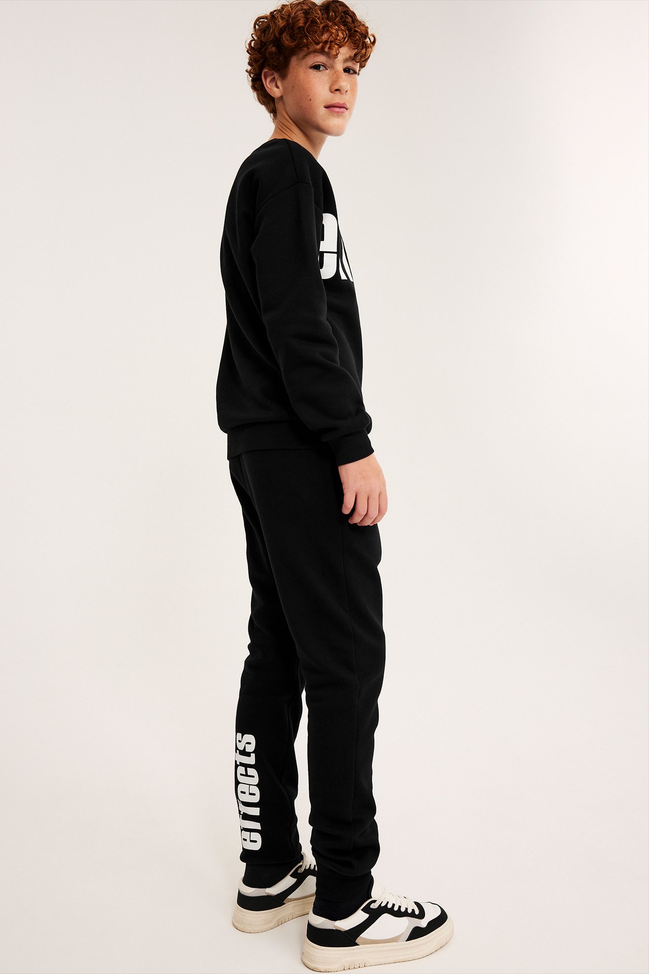 Sidebilde av barn i svart sweatshirt med hvitt trykk, svarte joggebukser 'effects' og sneakers.