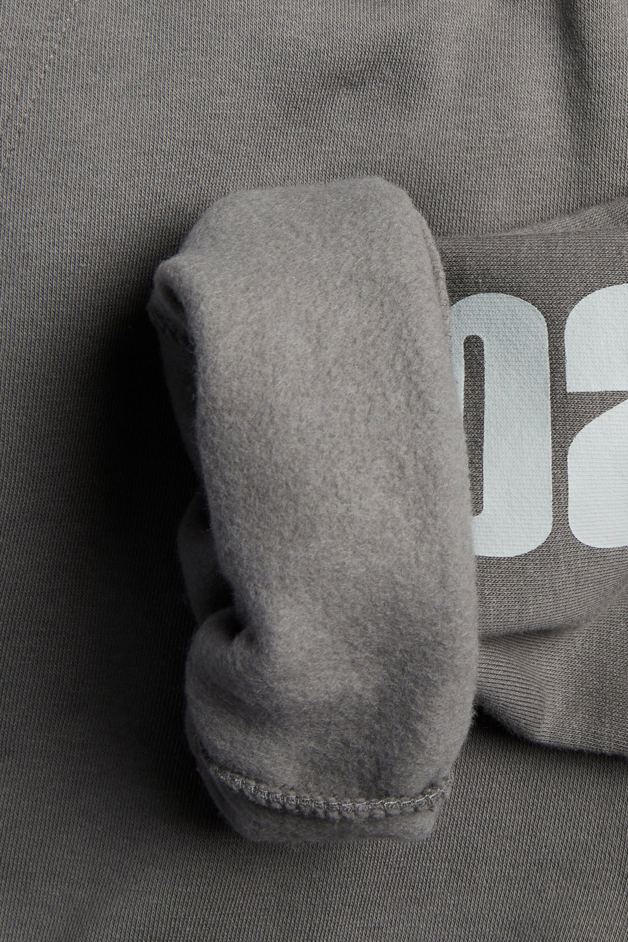 Zbliżenie na szarą bluzę z puszystą podszewką, dzianinowym spodem i białym nadrukiem.