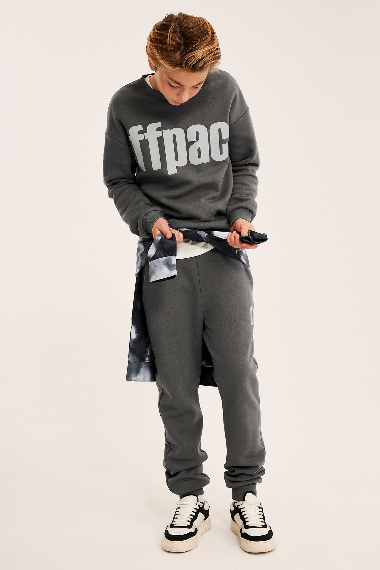 Barn iført mørkegrå 'ffpac' trykk genser, matchende joggebukse, batikkskjorte og joggesko, forfra.