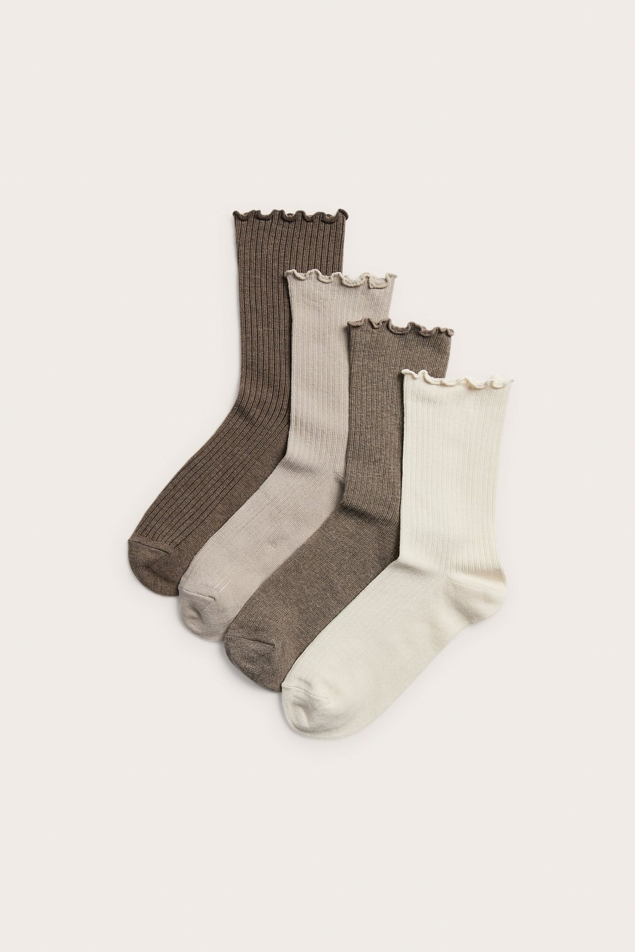 Uppifrån vy av fyra ribbstickade strumpor med volangkanter i brunt, taupe, mörkbeige och gräddvitt.