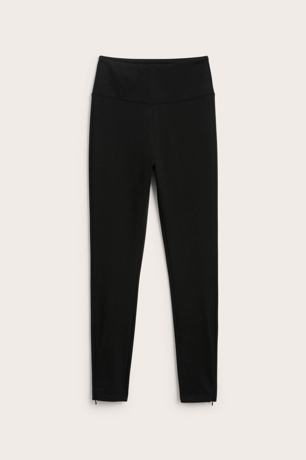 Edestä näkymä mustista, korkeavyötäröisistä capri-leggingseistä, joissa nilkkavetoketjut.