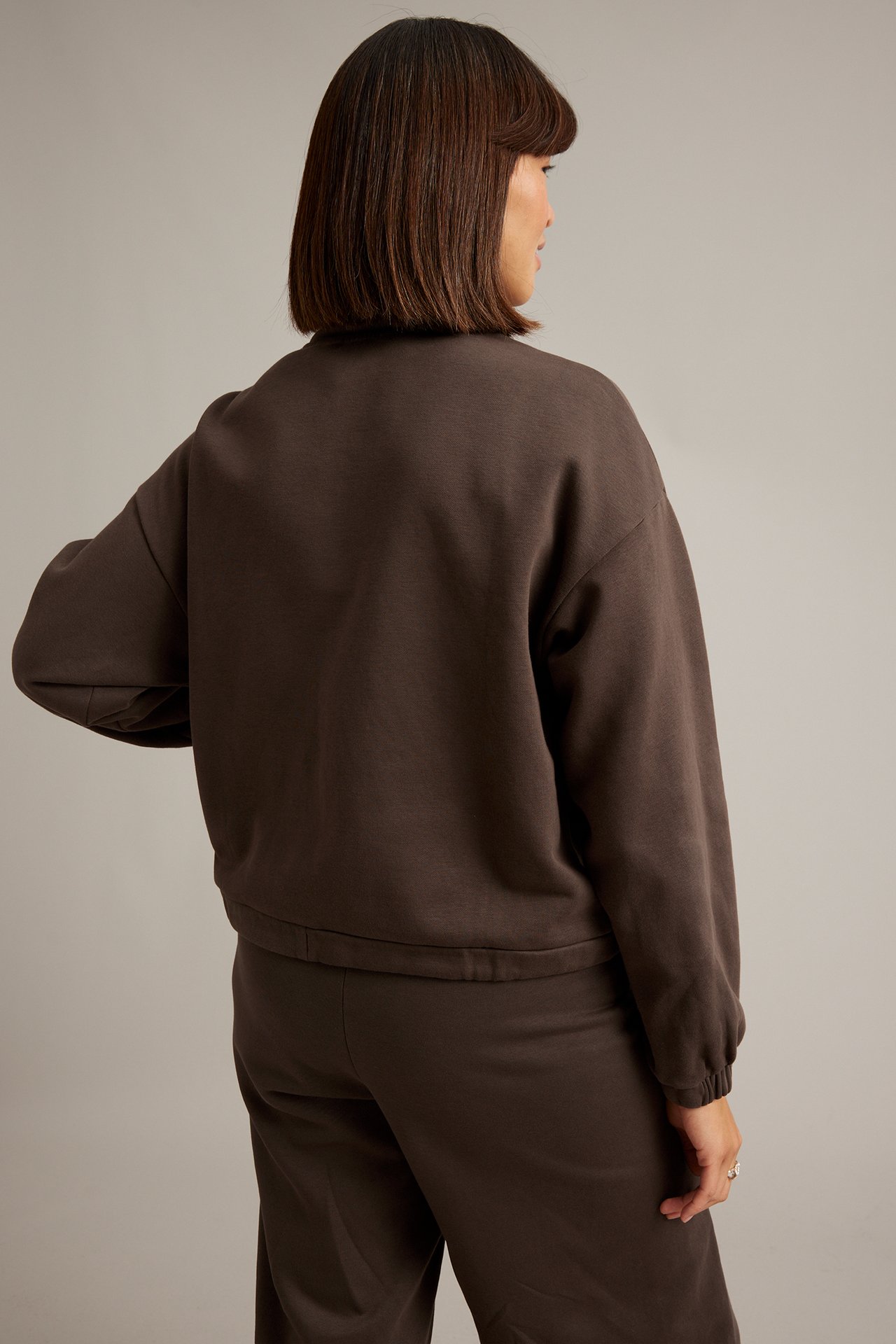 Bakifrån på kvinna i mörkbrun ledig tröja och matchande sweatpants.