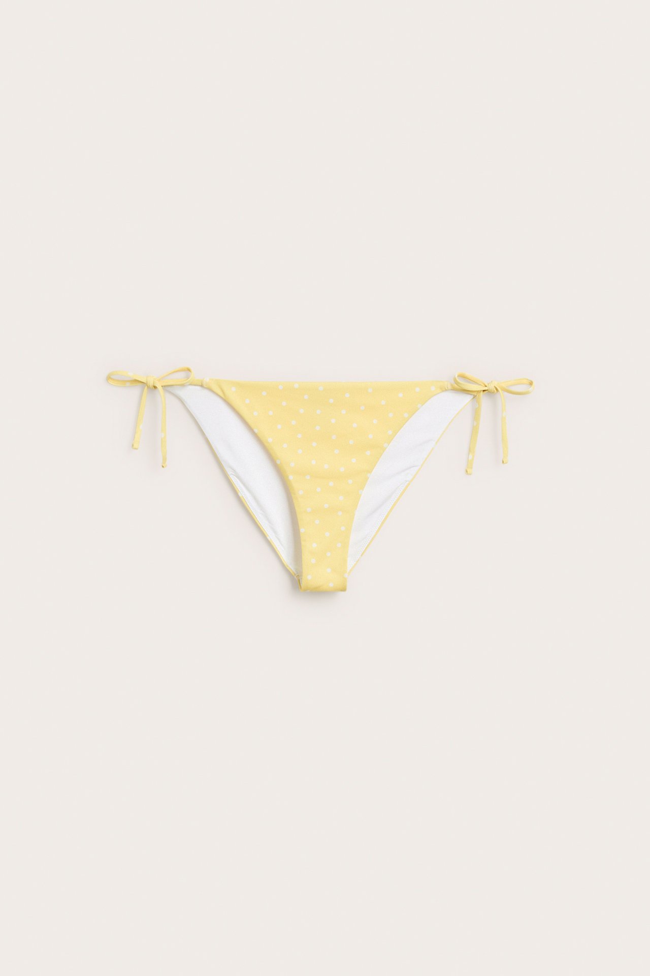 Forfra, gul brasiliansk bikinitruse med hvite prikker og knytebånd i sidene.