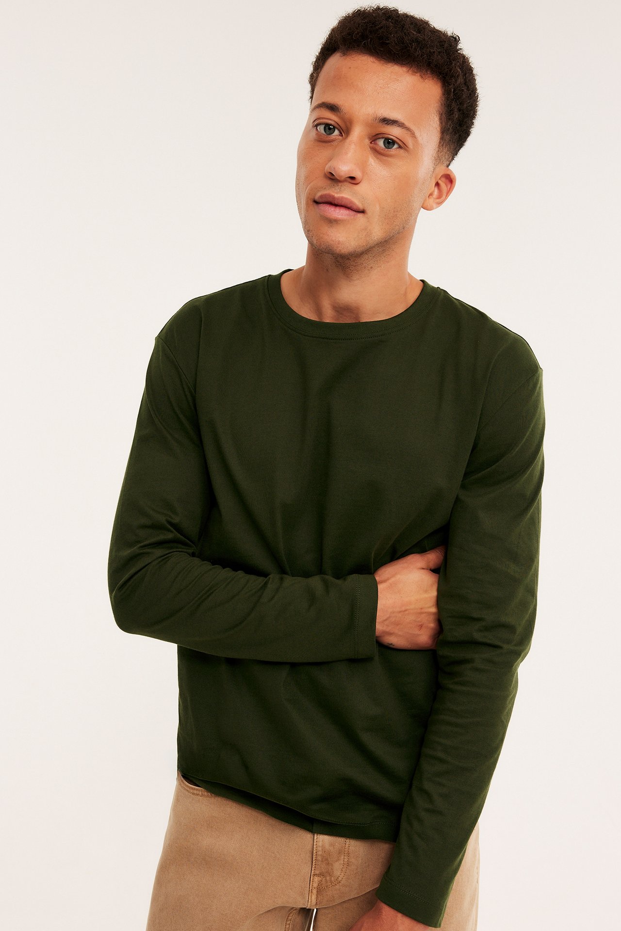 Framifrån, mörkgrön långärmad t-shirt med rund hals för herr, bärs med ljusbruna byxor.