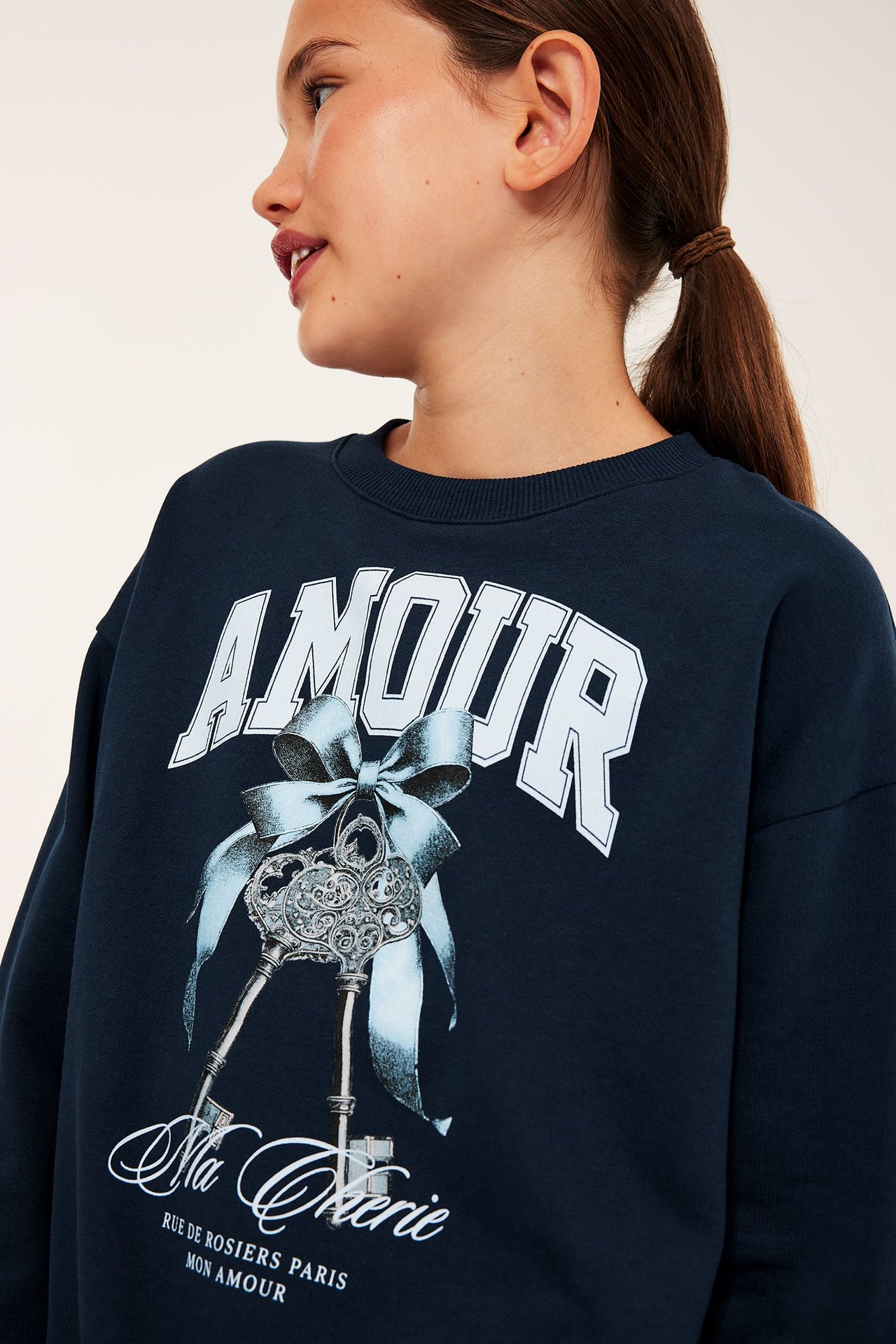 Närbild av barn i mörkblå sweatshirt med rund hals med 'AMOUR'-text och nyckelmotiv.