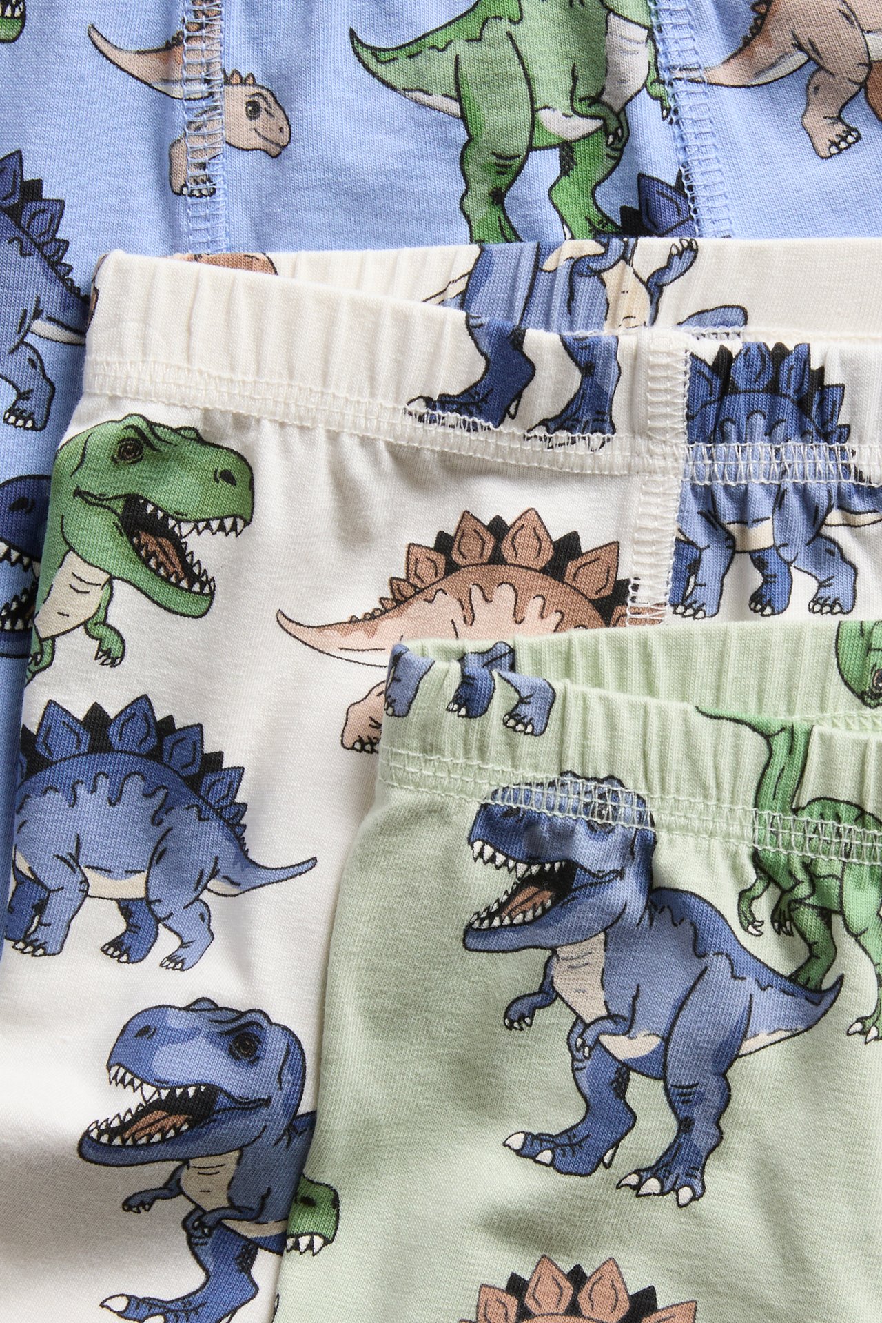 Närbild på tre par barnboxershorts med dinosaurietryck i blått, vitt och grönt.