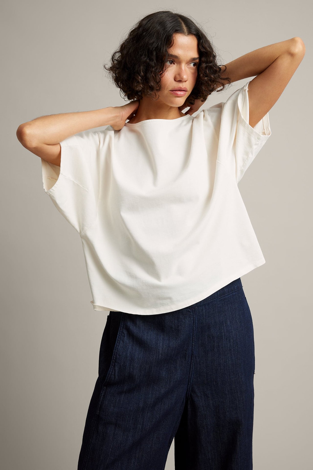Framsida av kvinnlig modell i gräddvit lös kortärmad topp med båthals och mörkblå vida jeans.