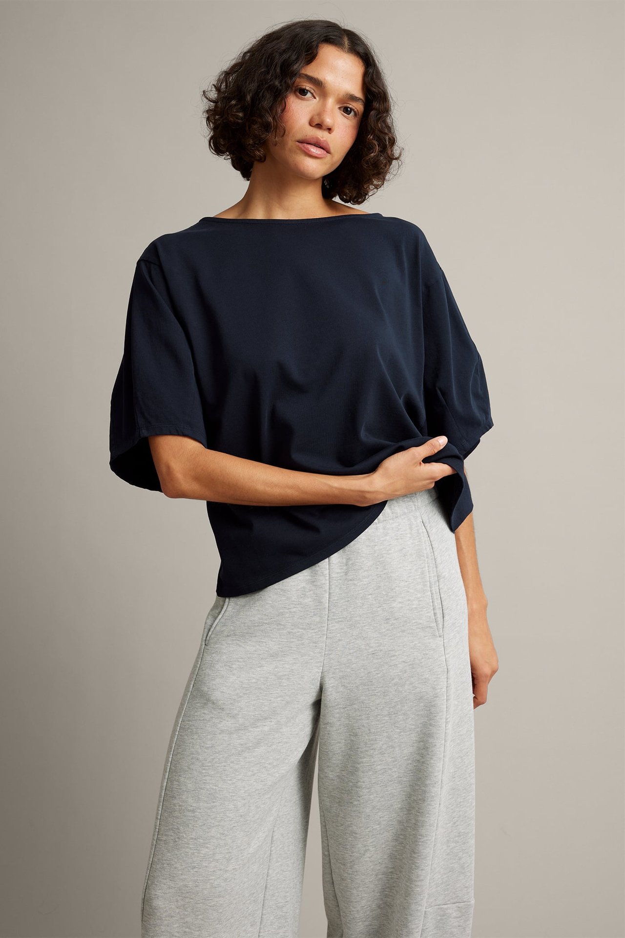 Widok z przodu kobiety w granatowym oversize'owym T-shircie z dekoltem łódkowym i jasnoszarych szerokich dresach.