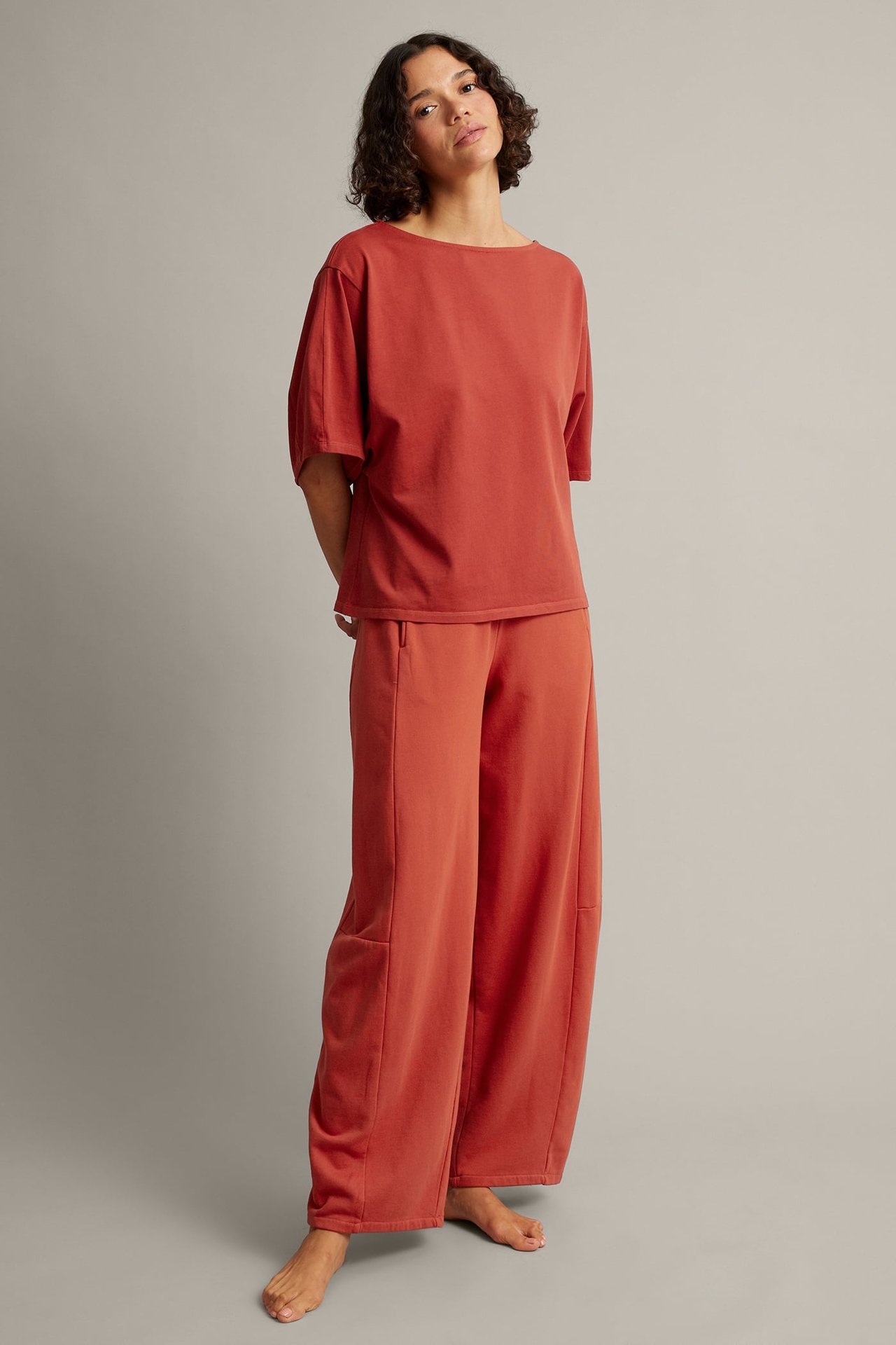 Frontvy: Kvinnlig modell i roströd kortärmad båthalsad topp och vida byxor.