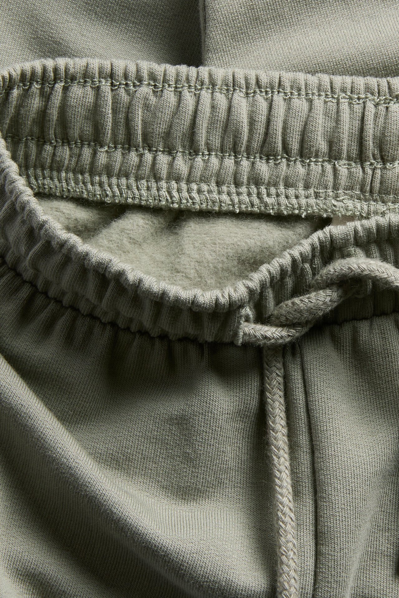 Nærbilde av salviegrønne joggebukser med elastisk linning og knytt snøring.