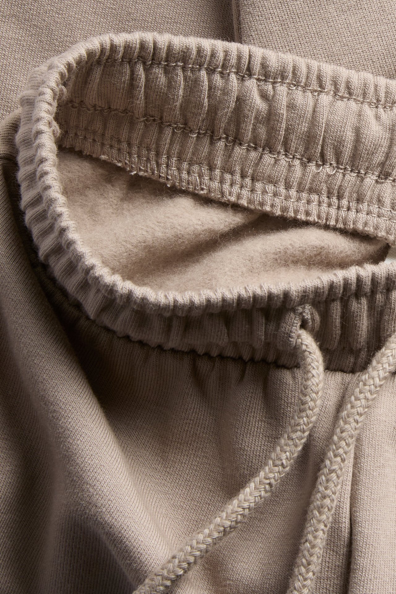 Nærbilde av beige fleecejoggebukse med elastisk midje og snøring.