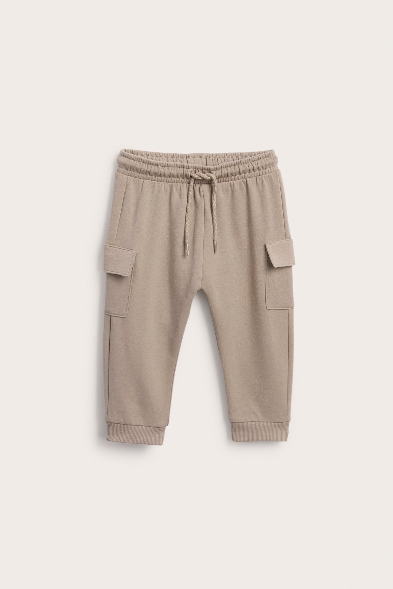 Frontal visning av barnas beige cargobukse med snøring og ribbekanter.