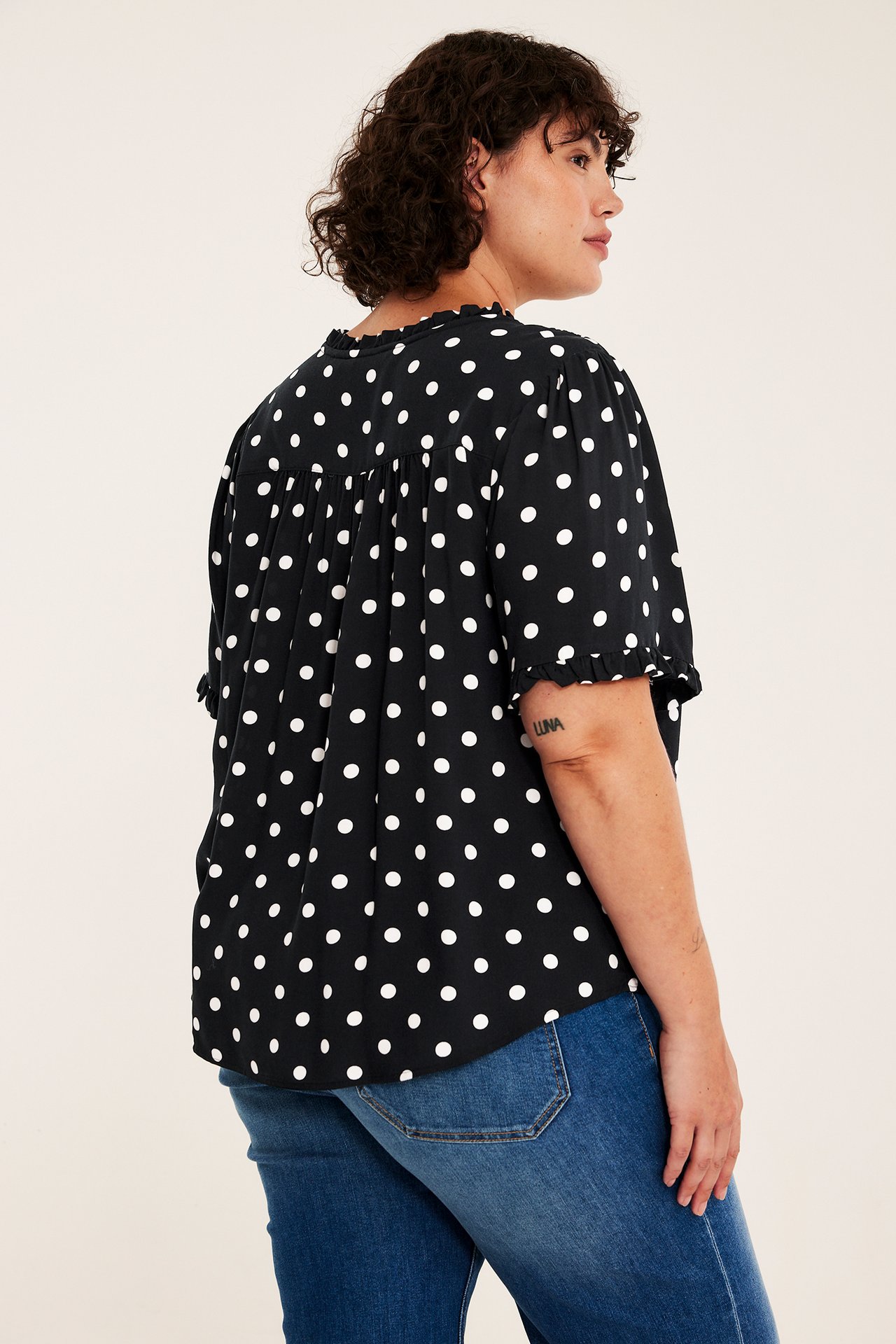 Side-bakfra visning av en kvinne i en svart kortermet prikkete topp og blå jeans.
