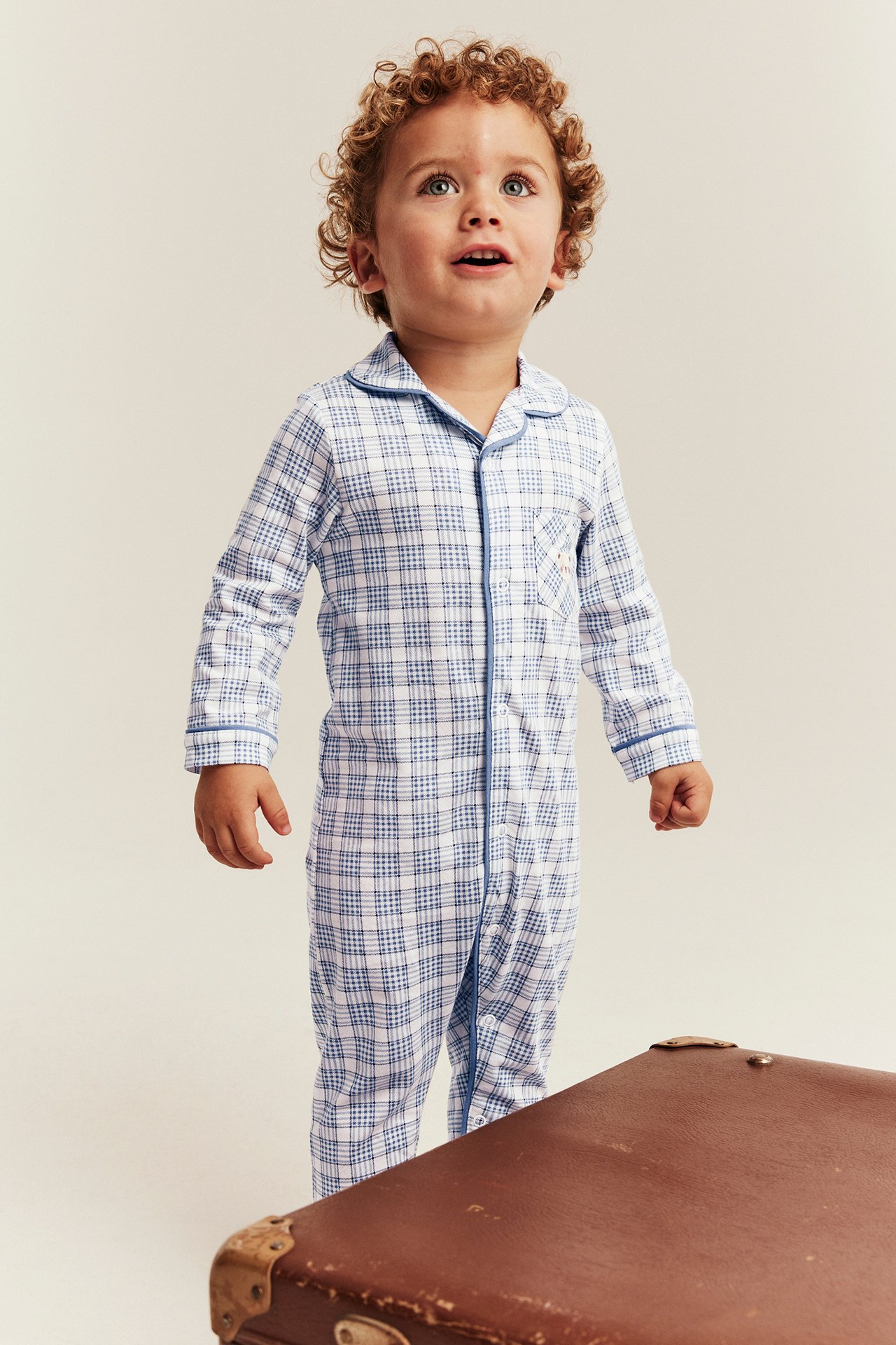 Edestä: lapsi sinivalkoruudullisessa yksiosaisessa pyjamassa kauluksella ja sinisellä reunuksella.