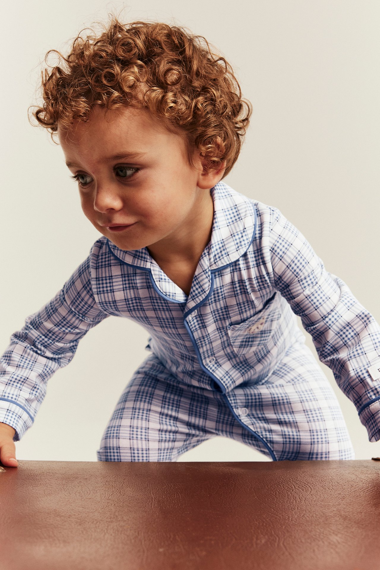 Edestä päin lapsi yllään sinivalkoruudulliset pitkähihaiset pyjamat sinisillä tereillä.