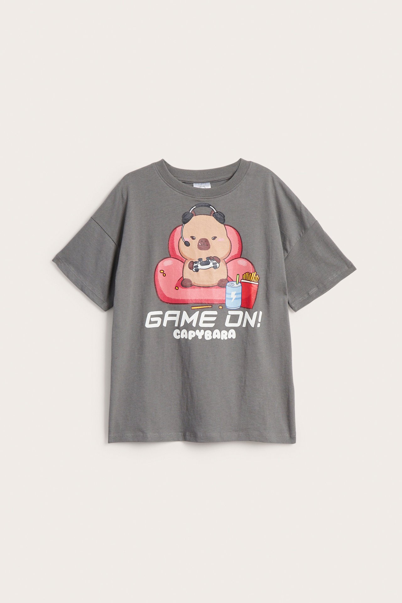 Z przodu, szary T-shirt oversize z nadrukiem kapibary grającej w gry i 'GAME ON!'.