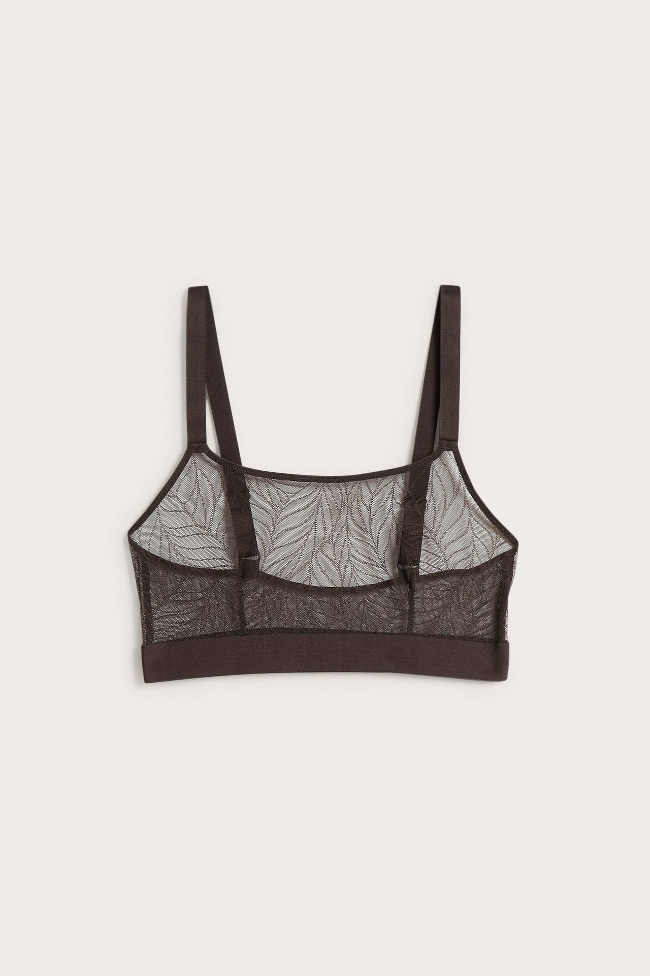 Baksidan av en mörkbrun mesh-bralette med lövmönster och justerbara axelband.