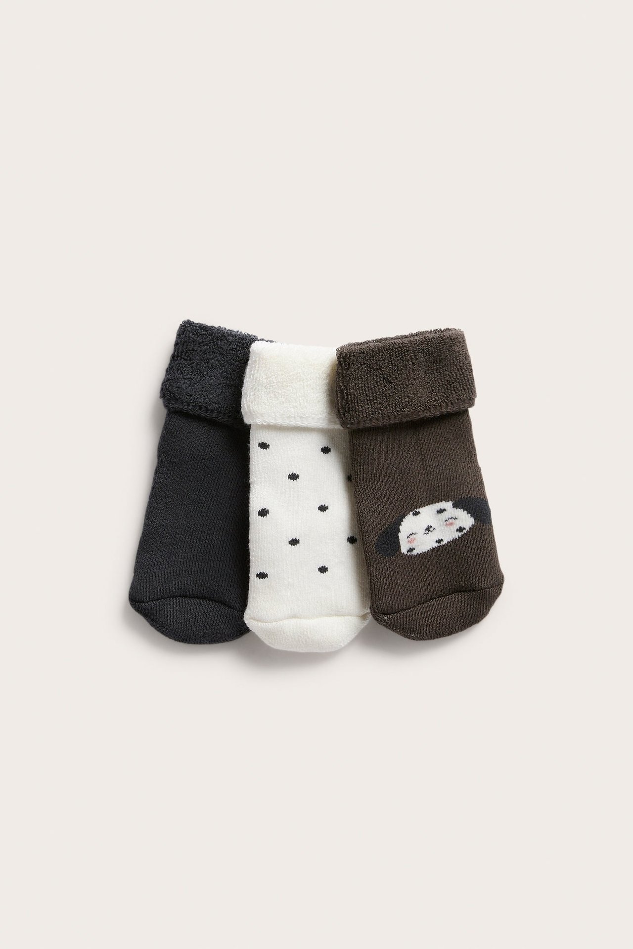 Framifrån tre baby strumpor: mörkgrå, vit prickig och brun med hundansikte.