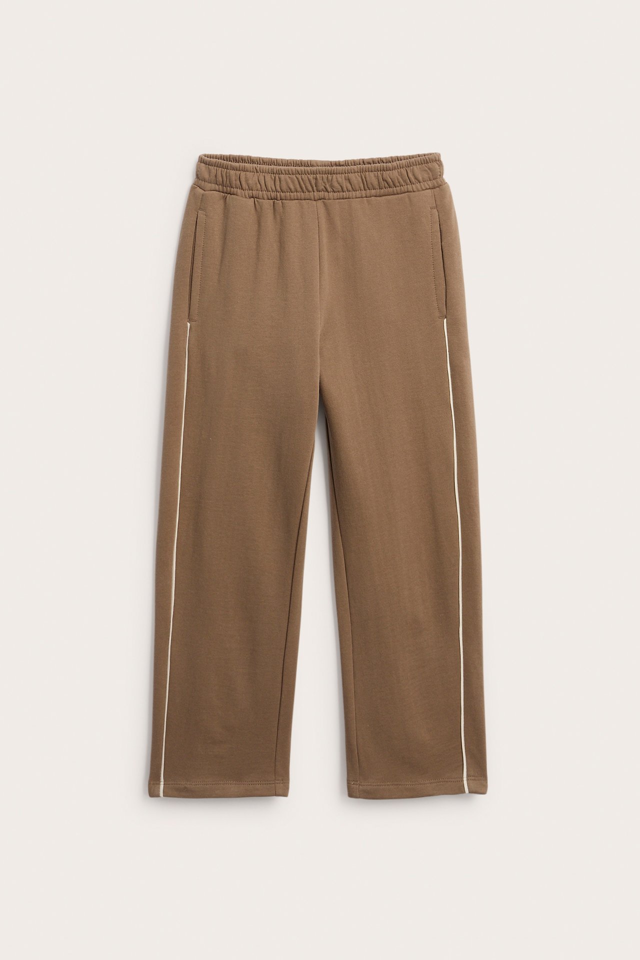 Frontbilde av brune joggebukser med elastisk midje, sidelommer og hvite sidestriper.