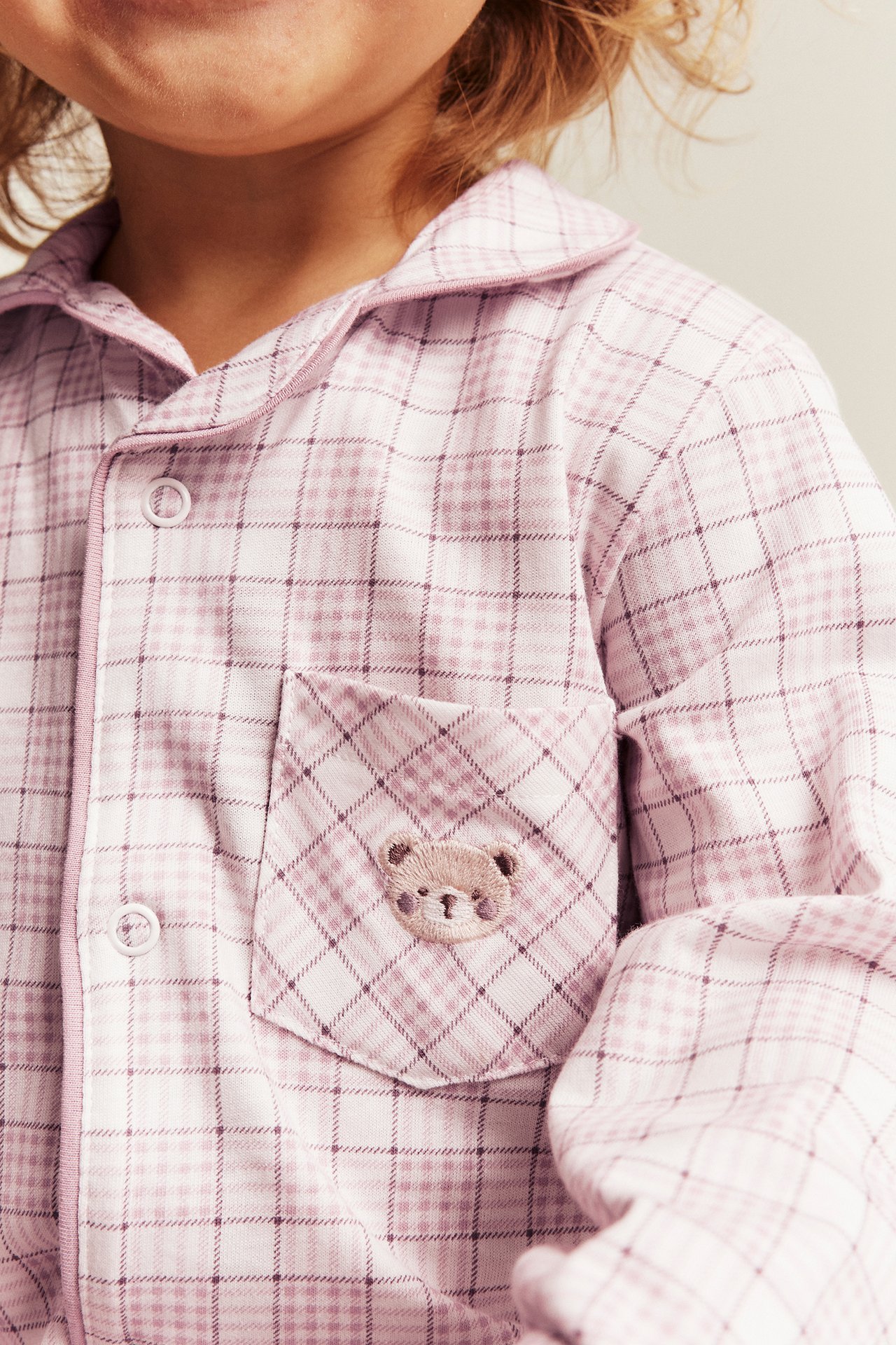 Lähikuva lapsesta vaaleanpunaisessa ruudullisessa pyjamapaidassa, jossa nallebrodeeraus taskussa.