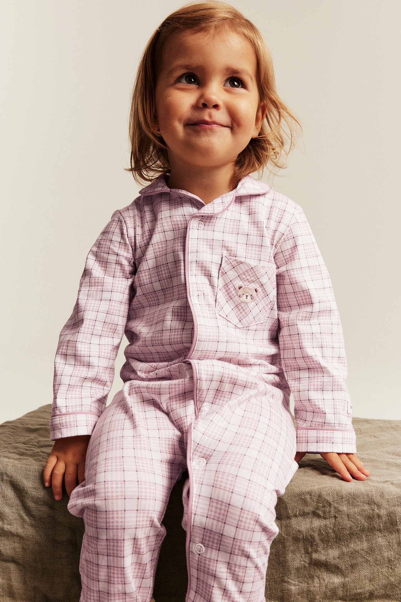Etunäkymä: Tyttölapsi yllään pinkki ruudullinen pyjama kauluksella ja kirjotulla karhutaskulla.