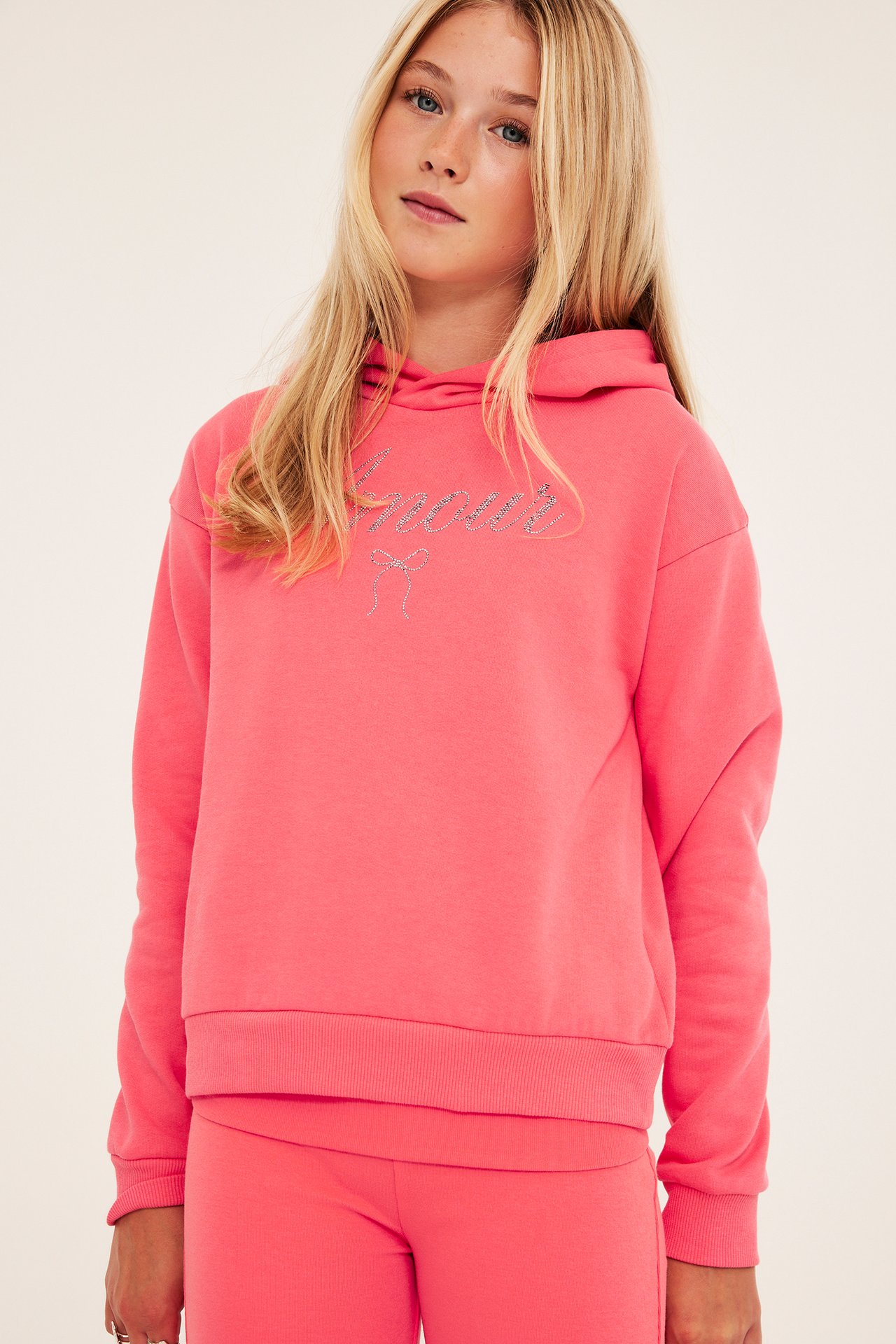 Framifrån, barn i rosa Amour-hoodie med rosett och matchande rosa leggings.