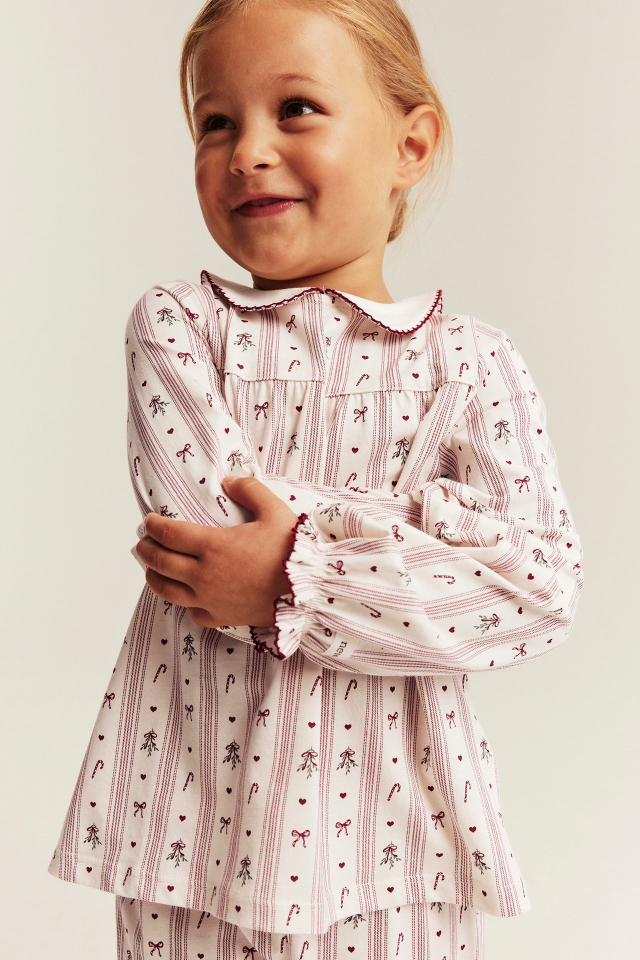 Framsida av barns vit långärmad pyjamastopp med röda ränder, jultryck och volangdetaljer.