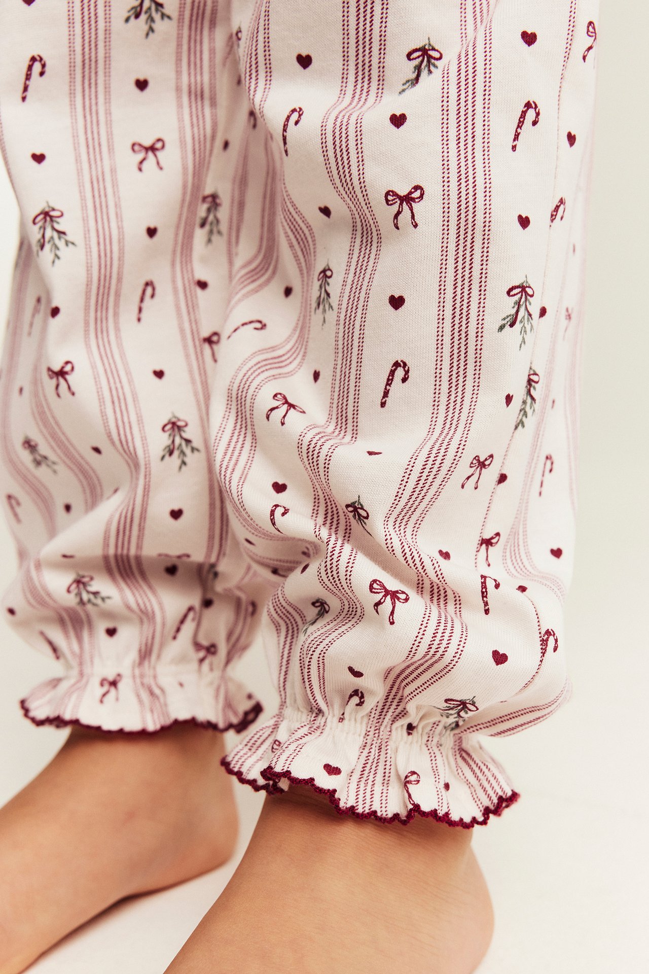 Närbild på vita pyjamasbyxor med röda ränder, hjärtan, rosetter, polkagrisar och volangmuddar.