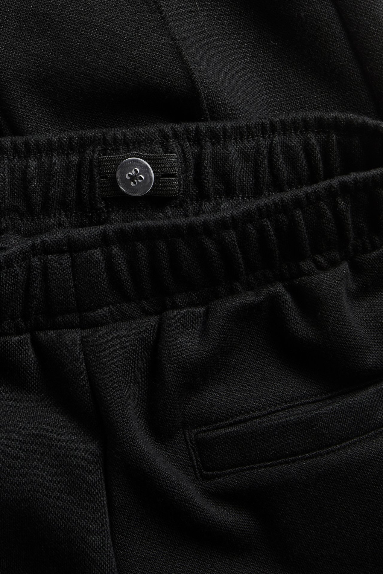 Närbild på svarta sweatpants med resår i midjan, justerbar knappflik och bakficka.