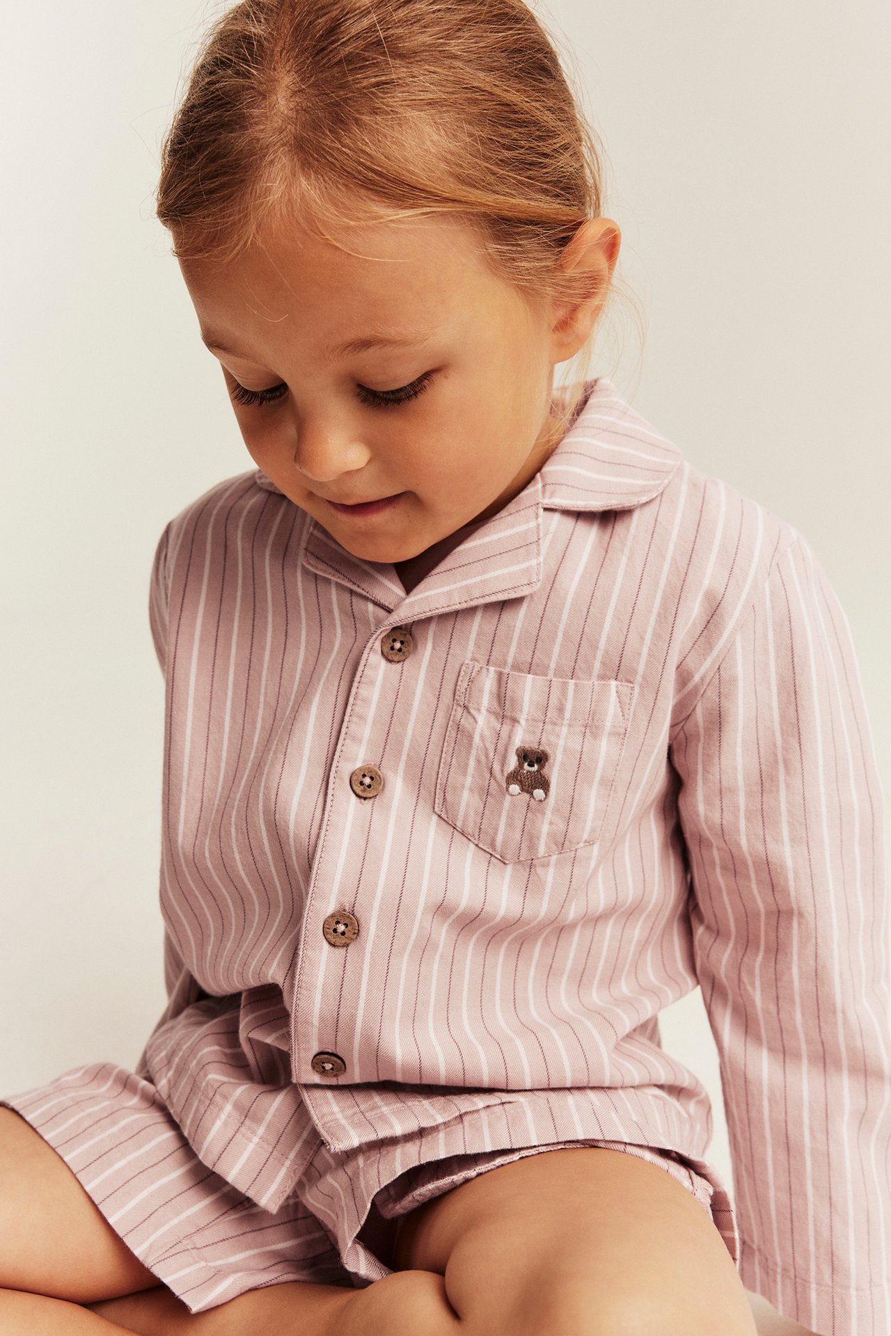 Närbild på barn i rosa randig pyjamasskjorta och shorts med broderad nallebjörn.