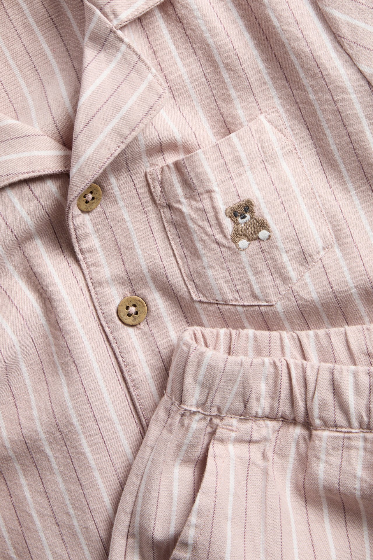 Närbild på ett rosa randigt pyjamasset med knappar och en broderad nallebjörn på fickan.