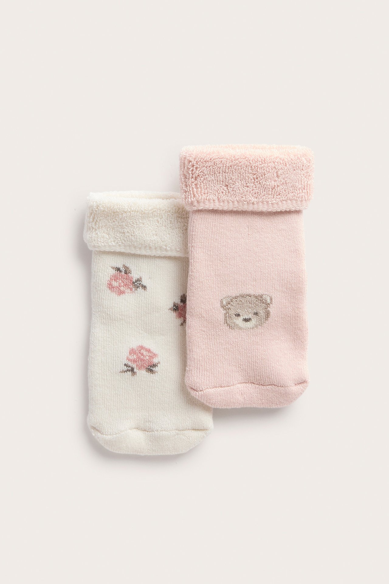 Nærbilde av babysokker; ett par rosa med bamse, ett par off-white med roser.