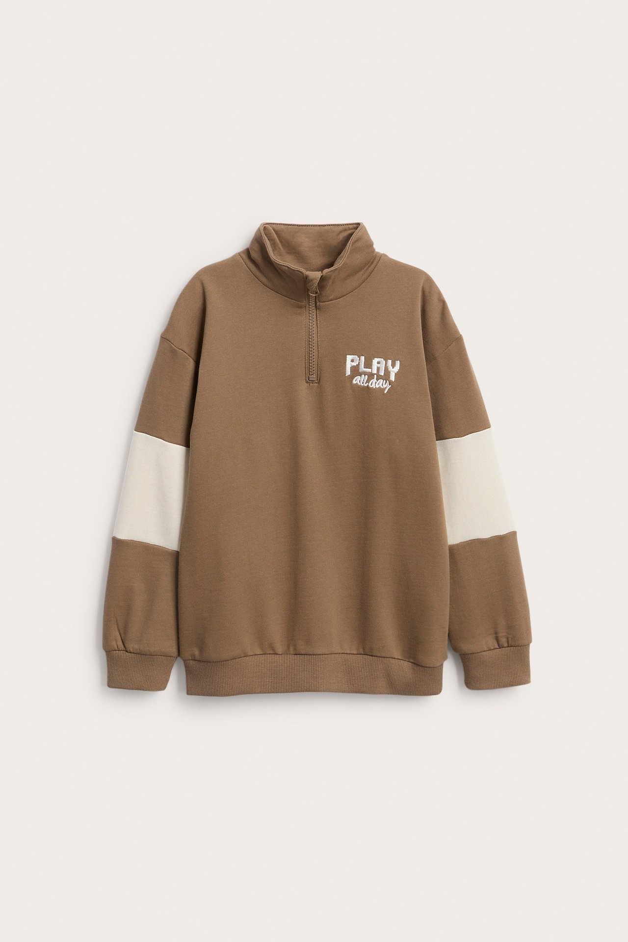 Edestäpäin, ruskea quarter-zip collegepaita kermanvärisillä hihoilla ja PLAY all day -painatuksella.